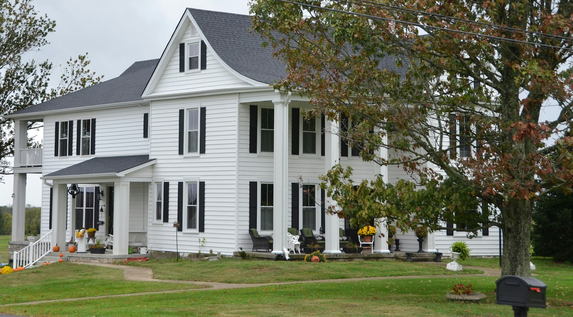 White farmhouse style home with tidy lawn and fall foliage, an example of fall curb appeal
