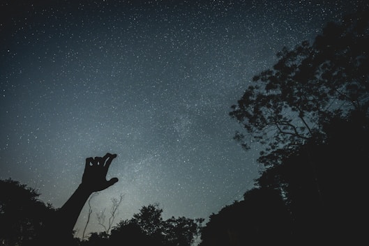 Silhouette of a hand reaching towards starry night sky