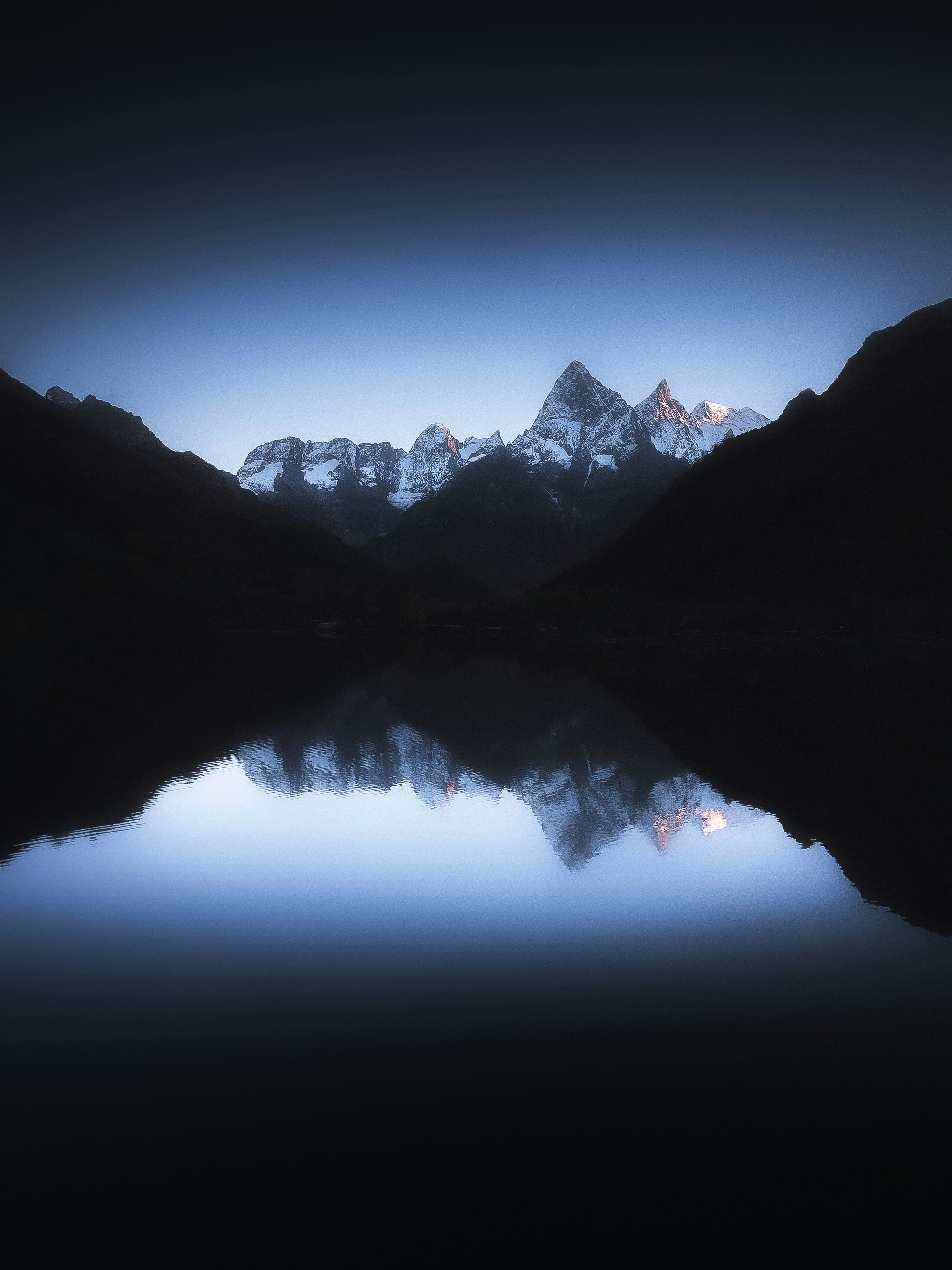 Montanhas cobertas de neve refletidas em um lago escuro ao entardecer