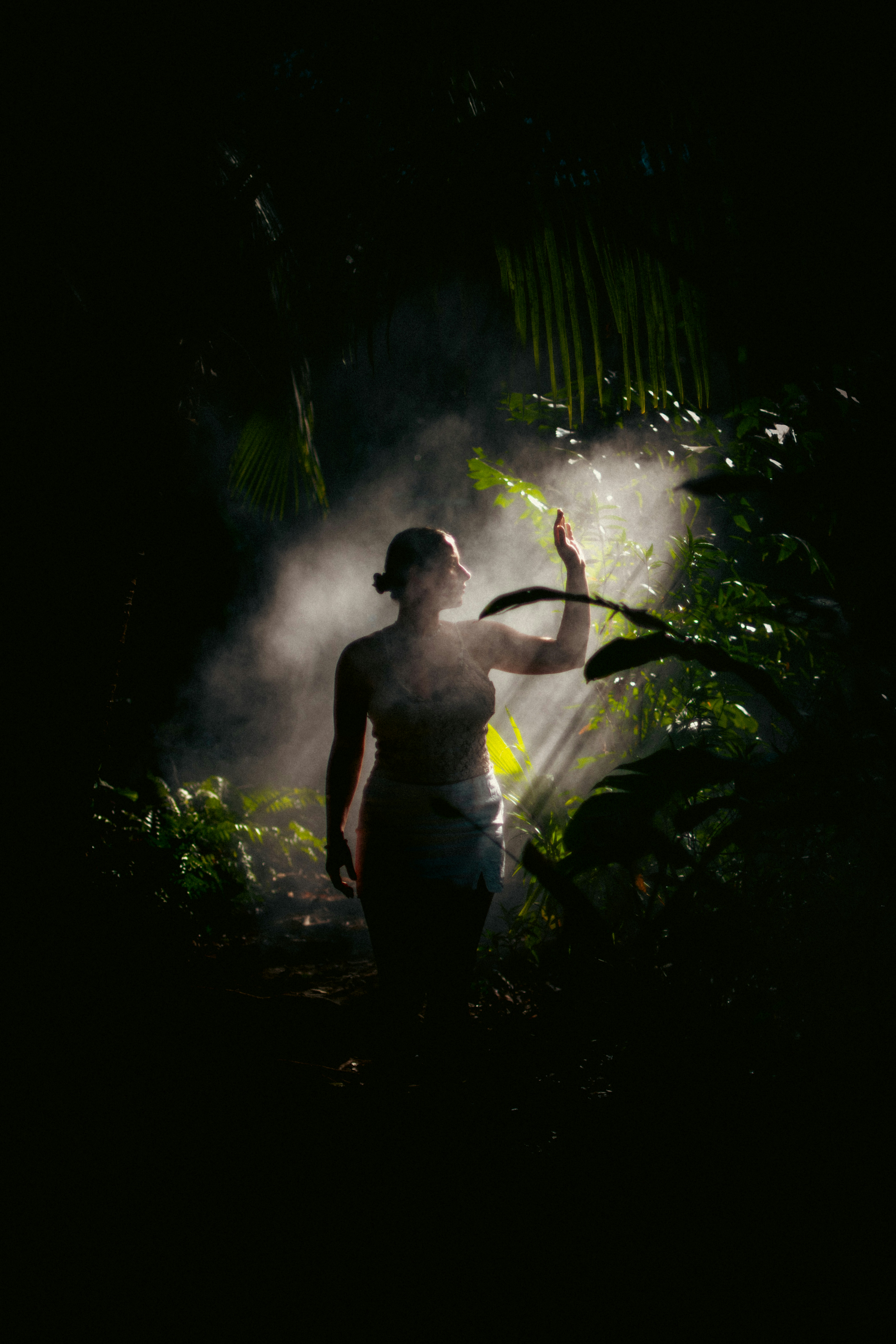 Woman walking through misty jungle with sunbeams in forest.