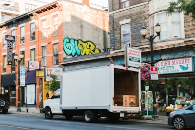 White truck parked on a city street with shops.