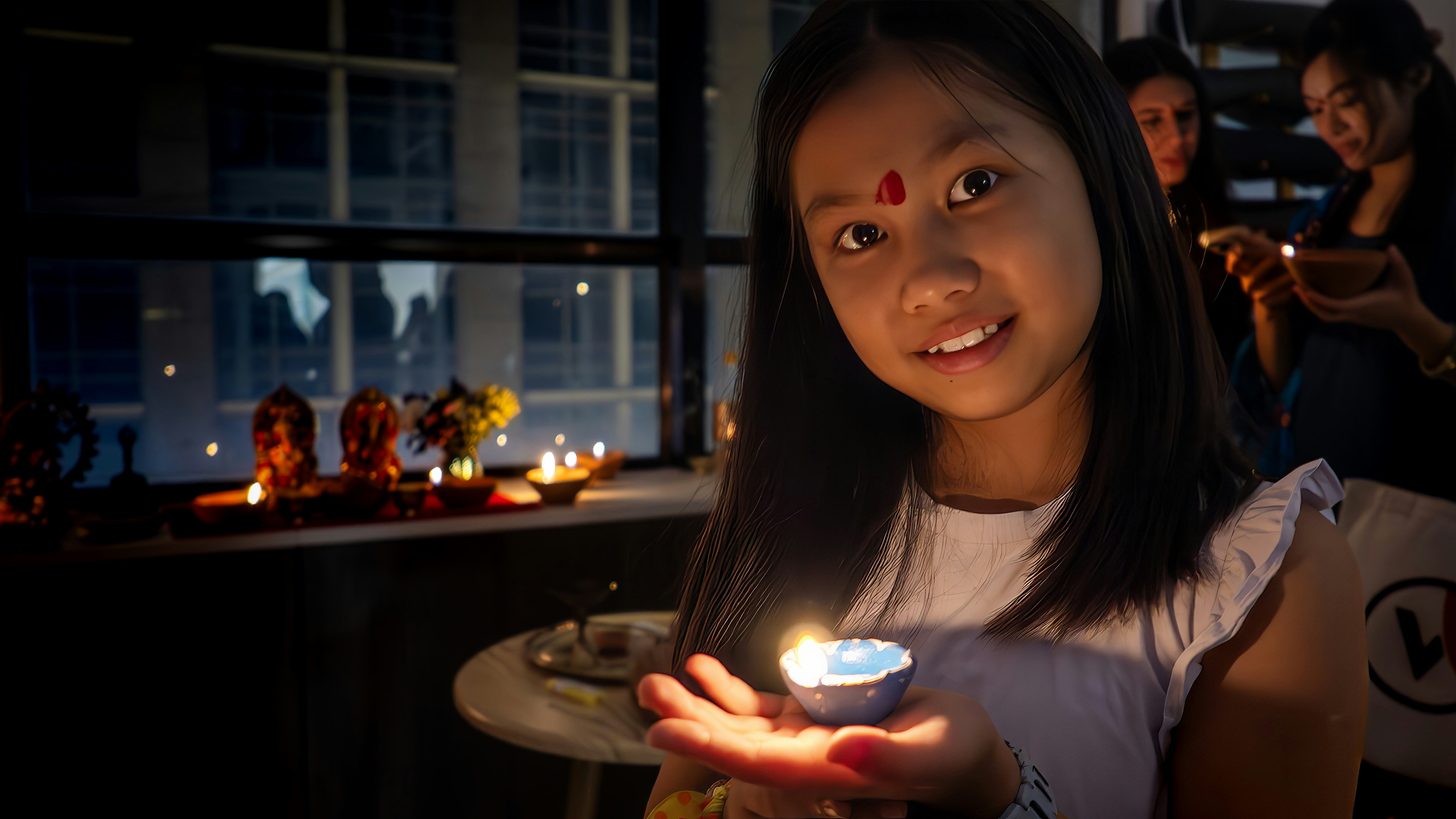Young girl holding a lit candle with diyas in darkness