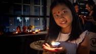 Young girl holding a lit candle with diyas in darkness