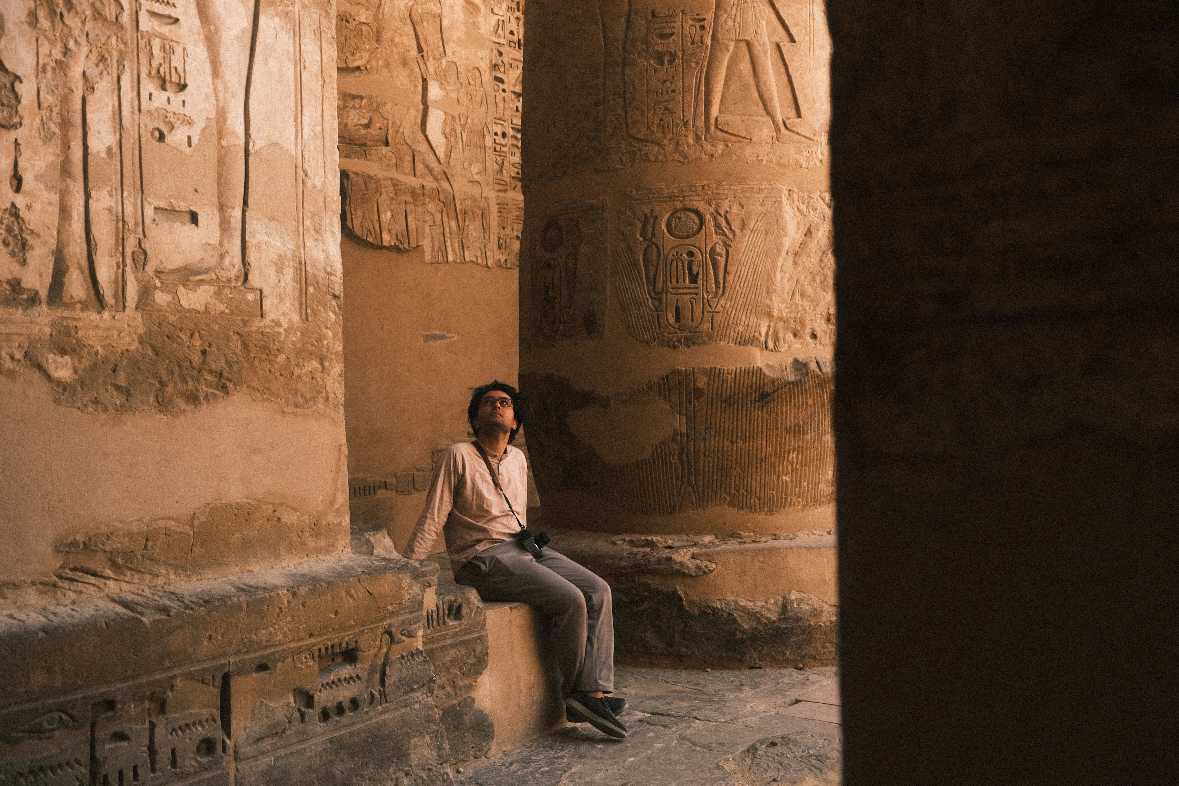 A visitor sits in the shade between the hieroglyph-carved column drums of Medinet Habu on the Luxor west bank, the sandstone glowing warm in late afternoon light.