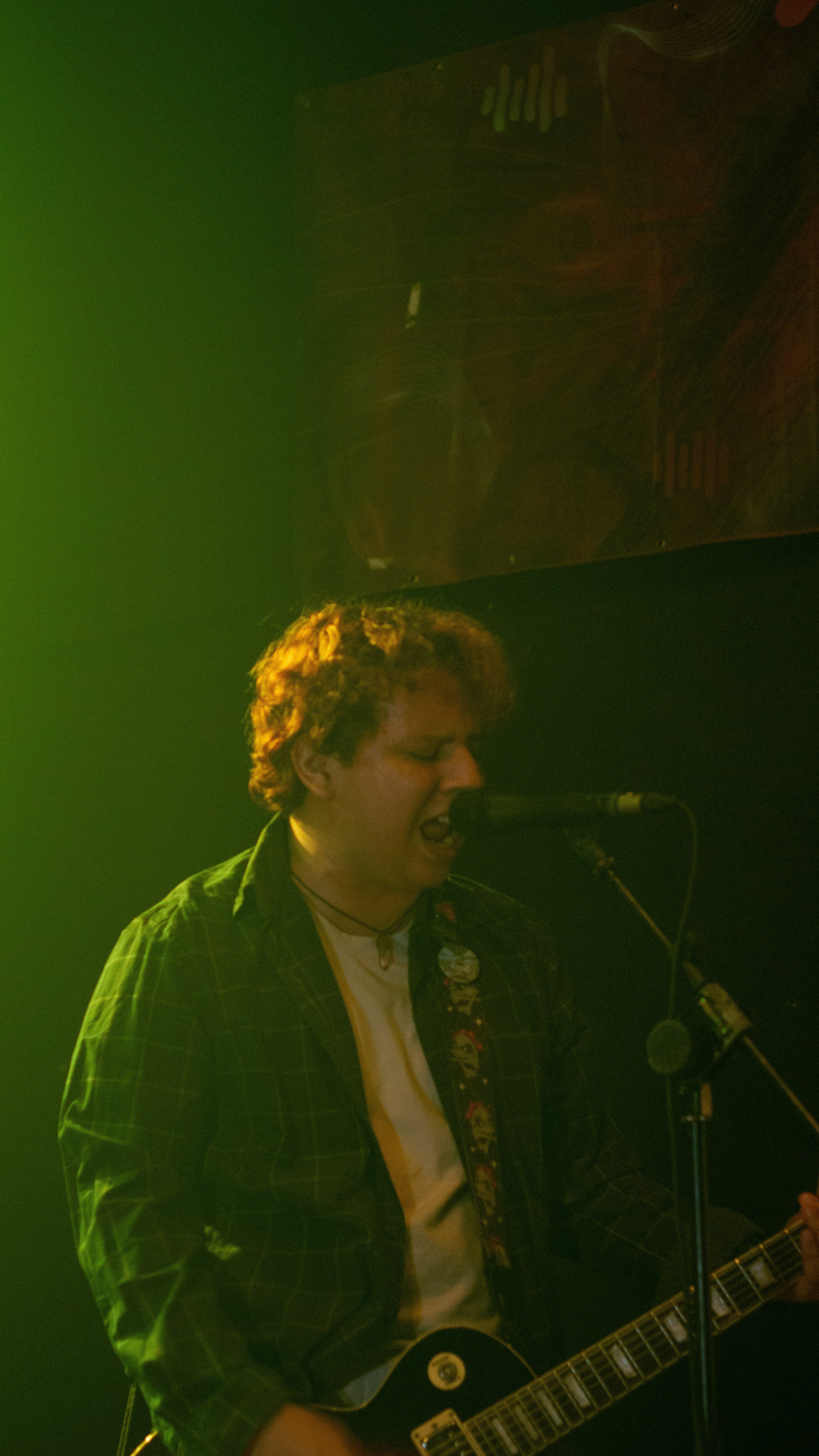 A man with curly hair playing guitar and singing.