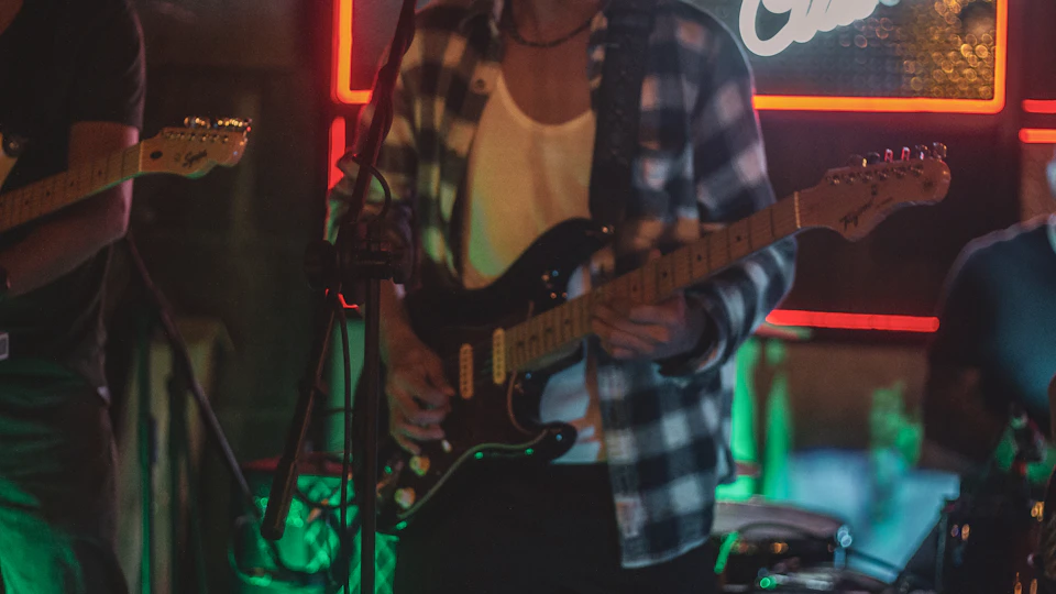 Musicians perform on stage with guitars and drums, wearing distinctive shirts and playing instruments