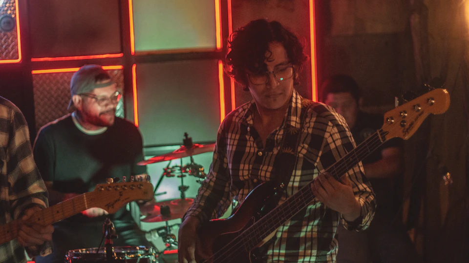 Two musicians perform live on stage with guitars and bass in a dimly lit room