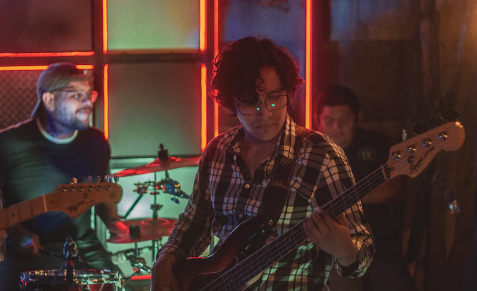Three musicians perform live on stage with neon-lit window background