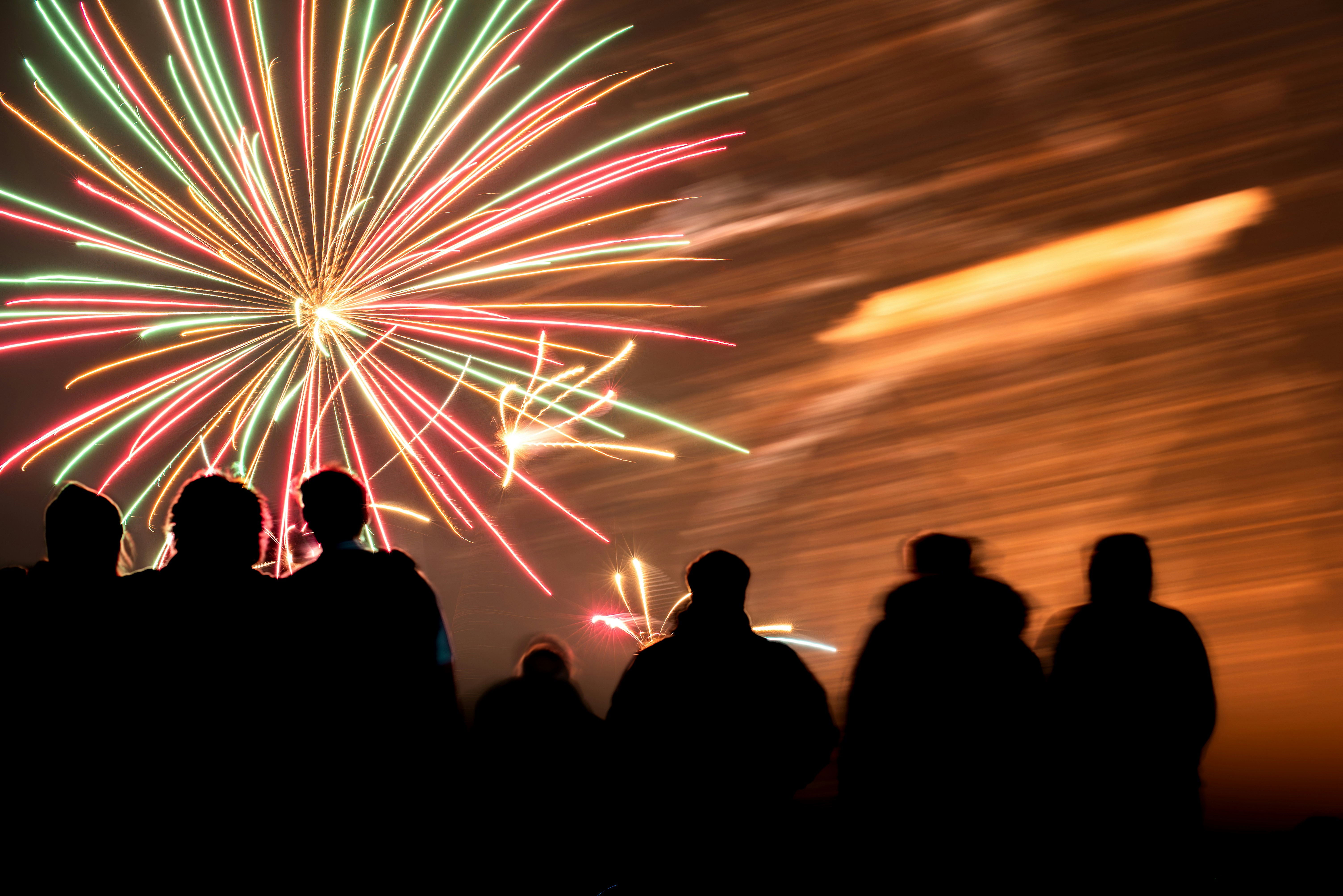 Silhouetted crowd watches colorful fireworks explode in night sky