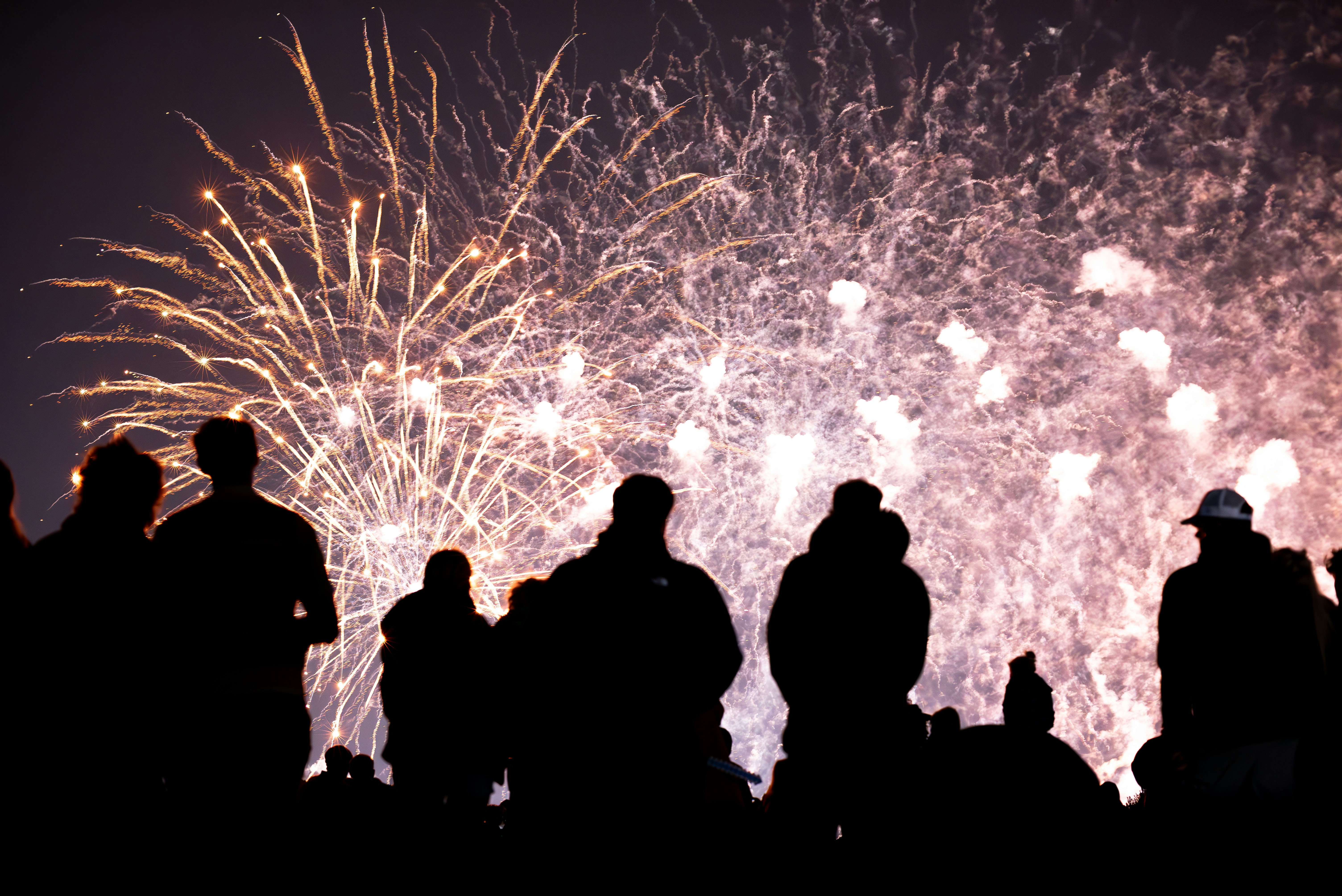 Silhouettes of people watching fireworks display at night.