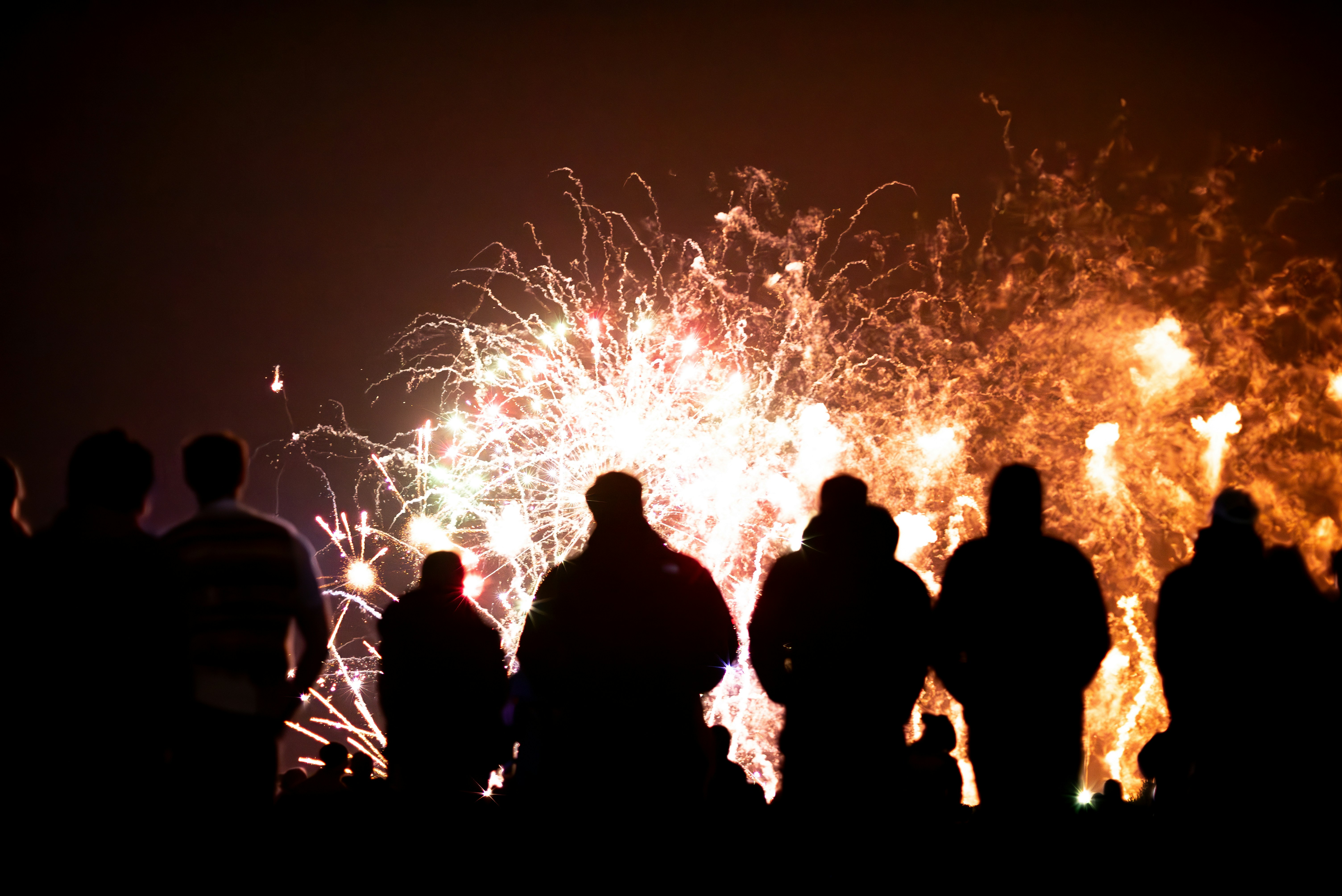 Silhouettes of people watching fireworks display at night