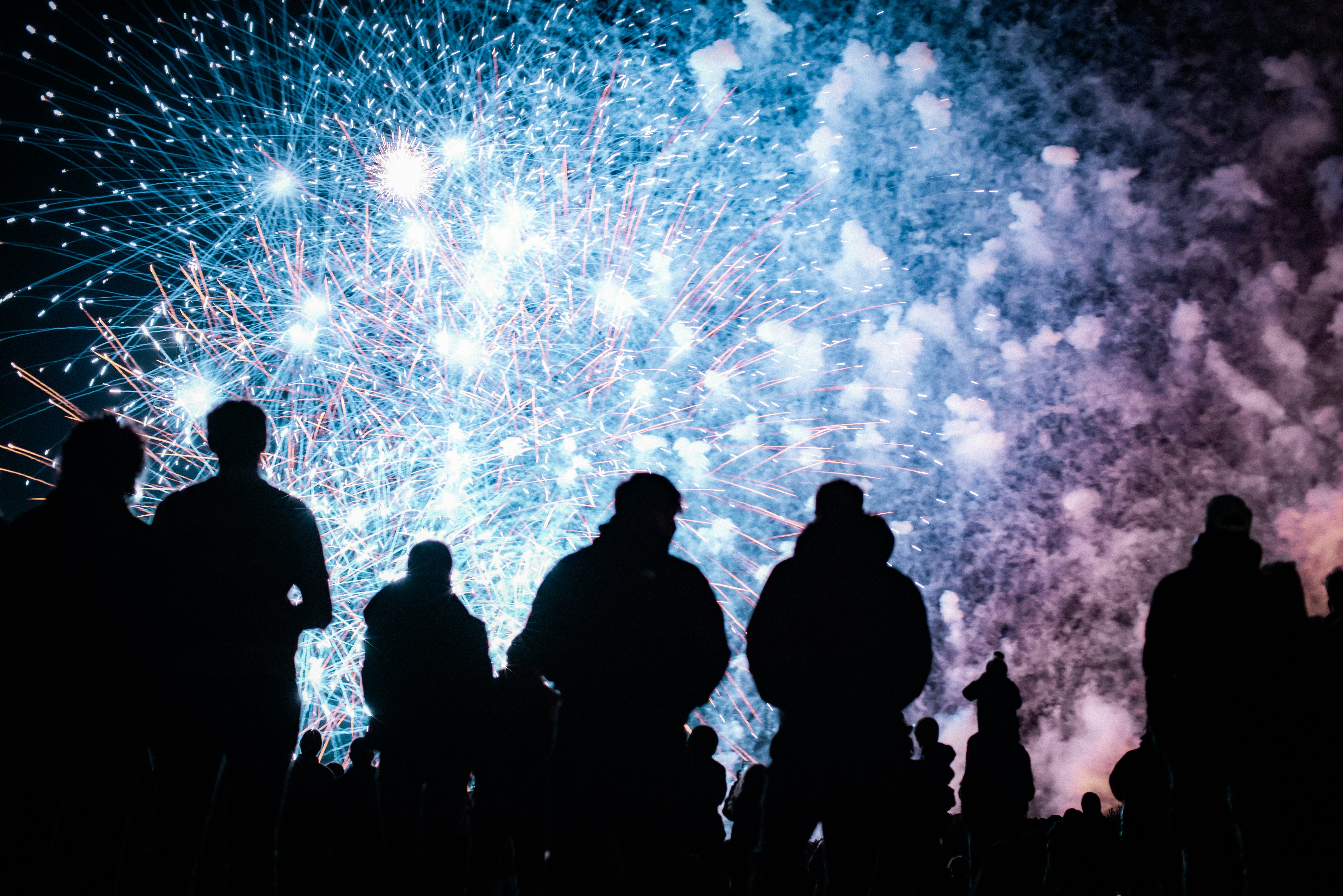 Silhouetted crowd watches colorful fireworks display at night.