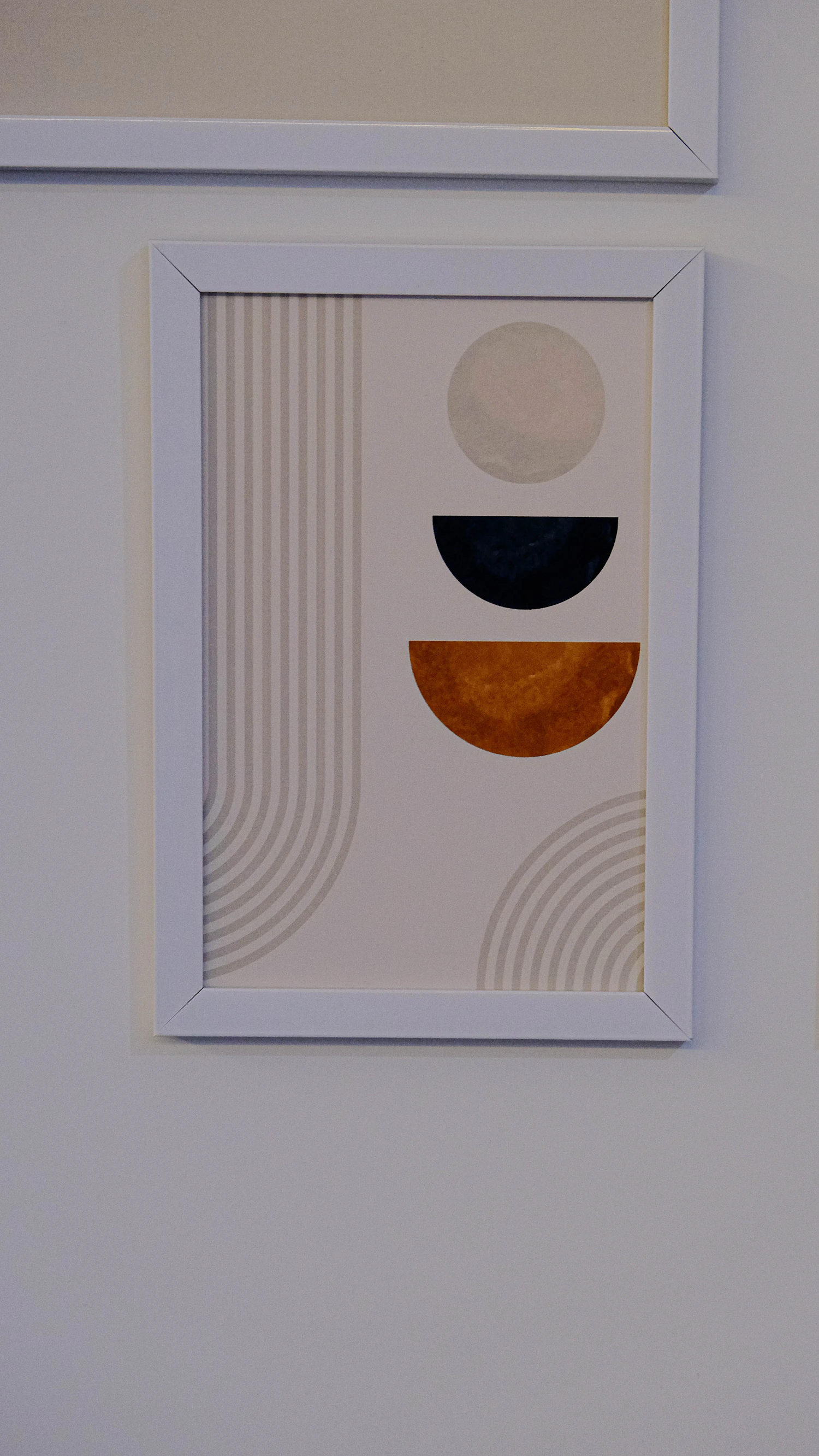 A geometric print with a black arch and orange half circle in a white frame on a light wall
