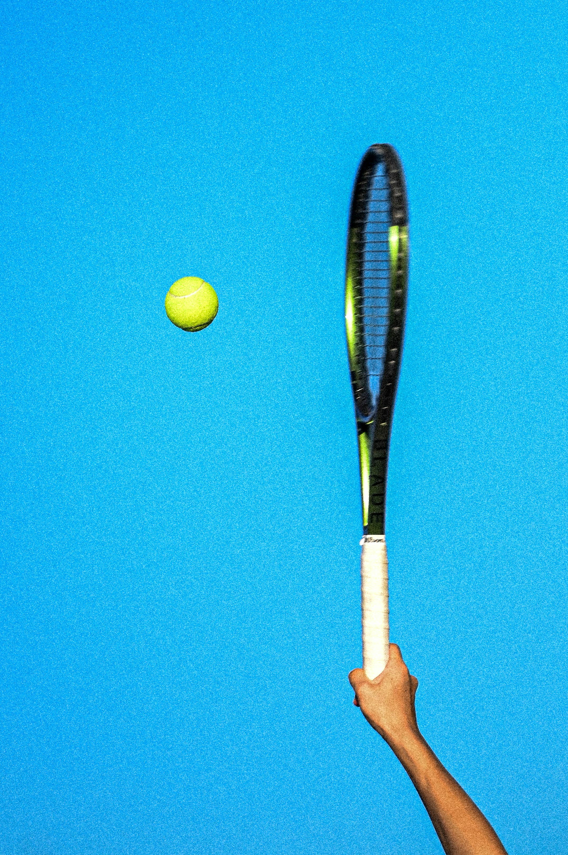 Mano sosteniendo la raqueta de tenis golpeando la pelota amarilla
