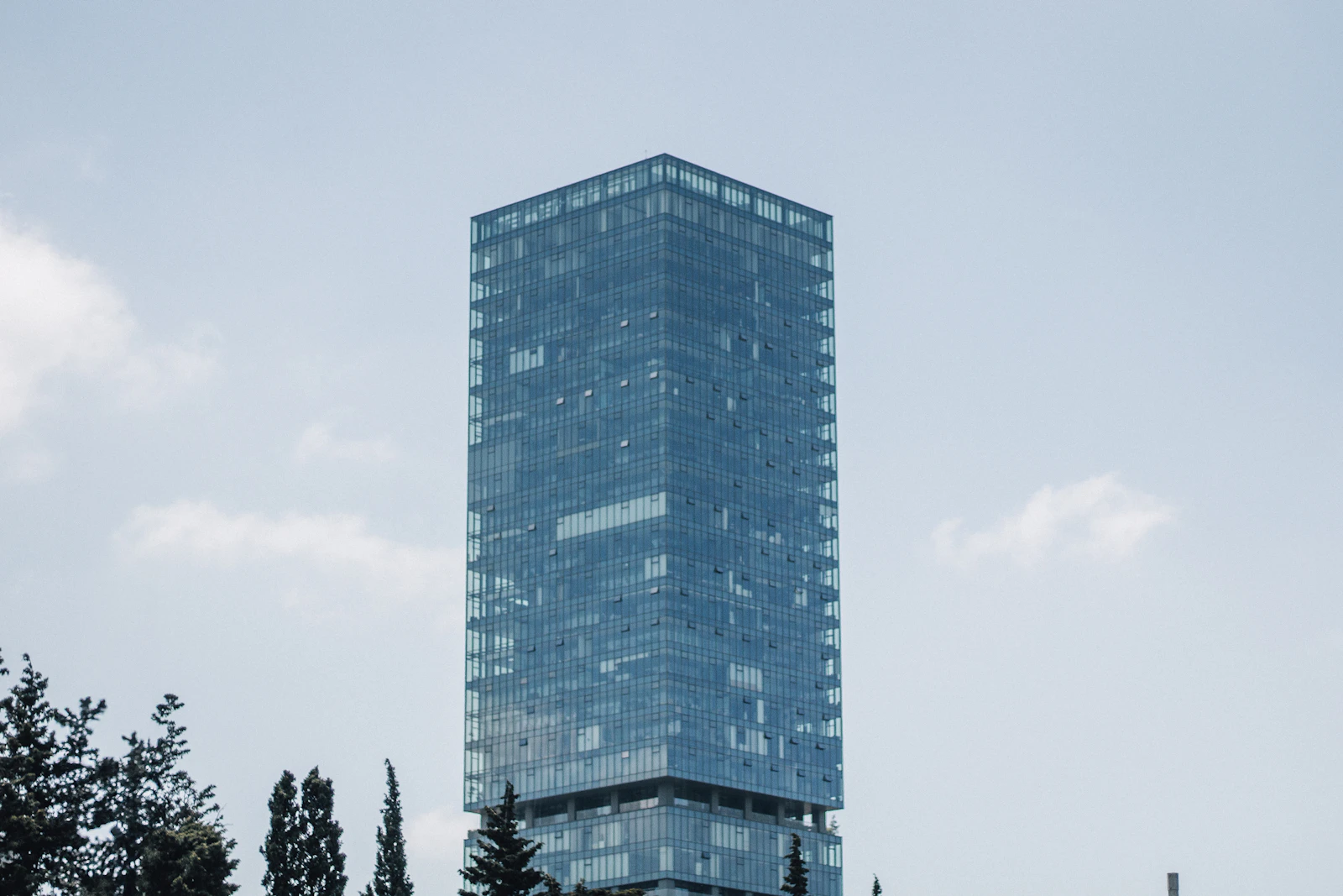A tall glass skyscraper rising into empty sky, corporate ambition rendered in steel and glass