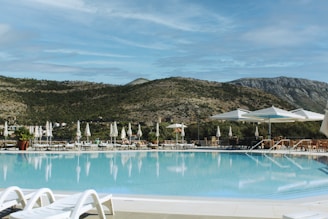 Resort swimming pool with lounge chairs and mountains.