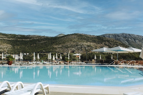 Resort swimming pool with lounge chairs and mountains.