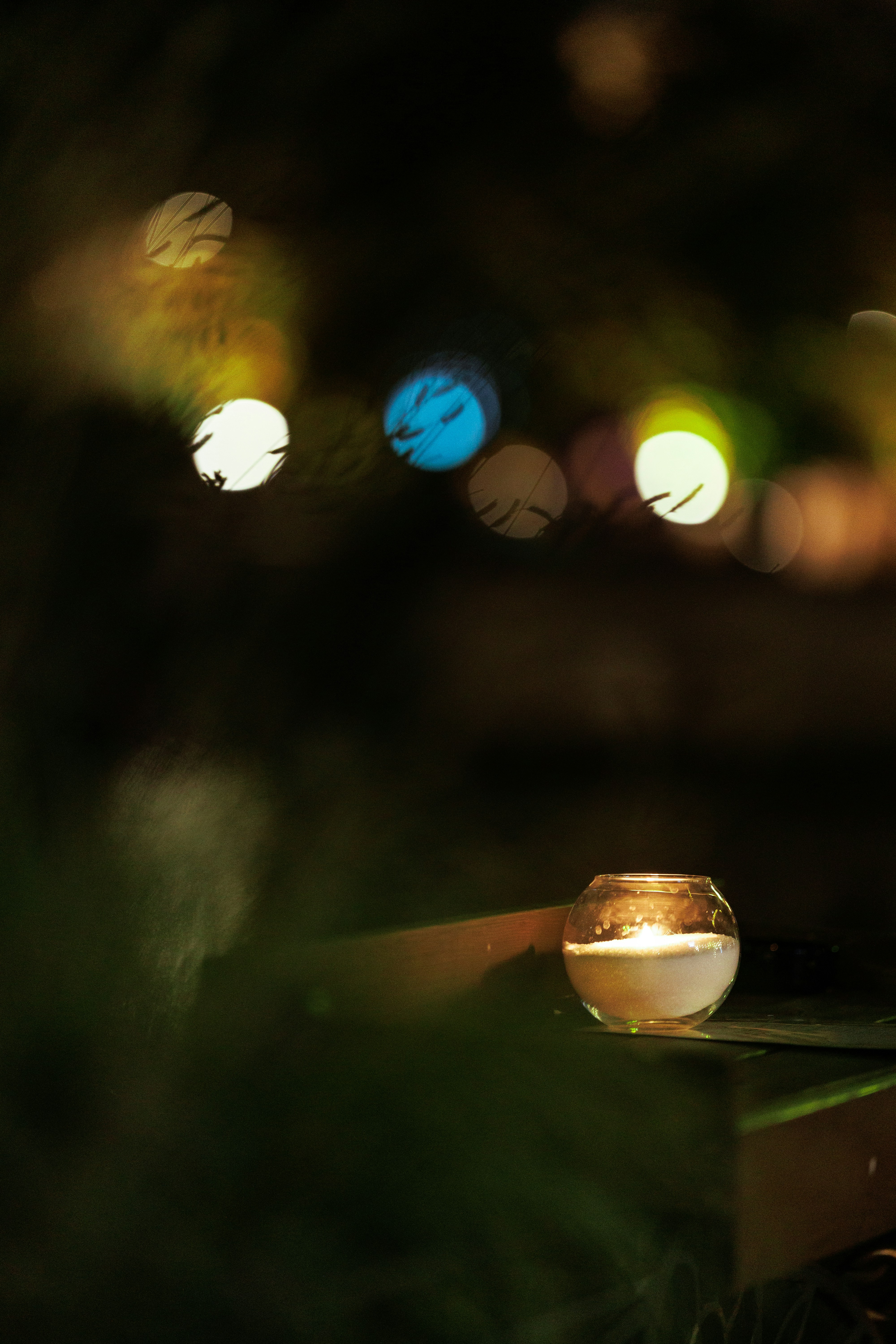 A lit candle in a glass holder at night.