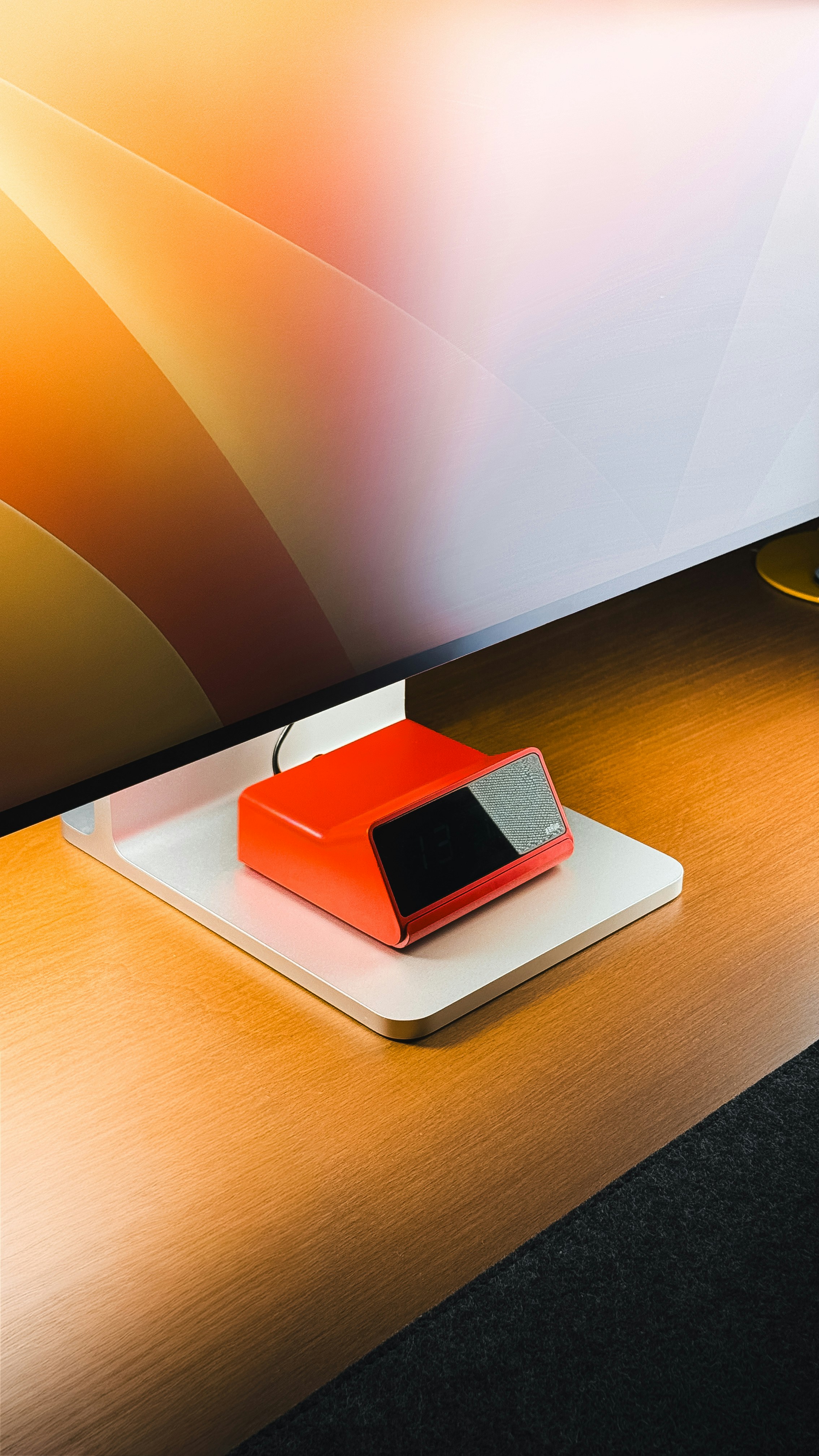 Red electronic device on a white stand on wooden desk