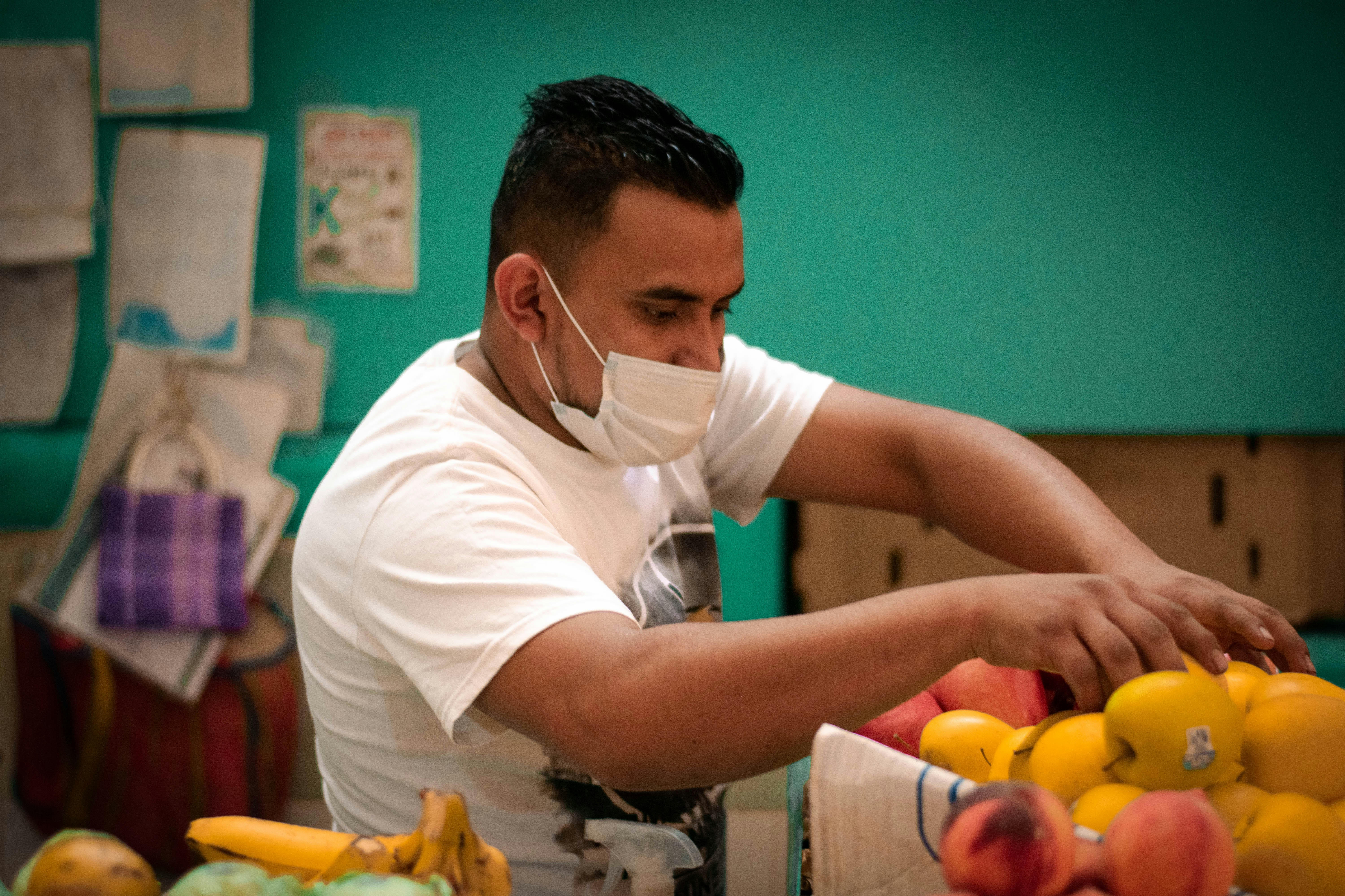 Man in mask arranging fruit at market