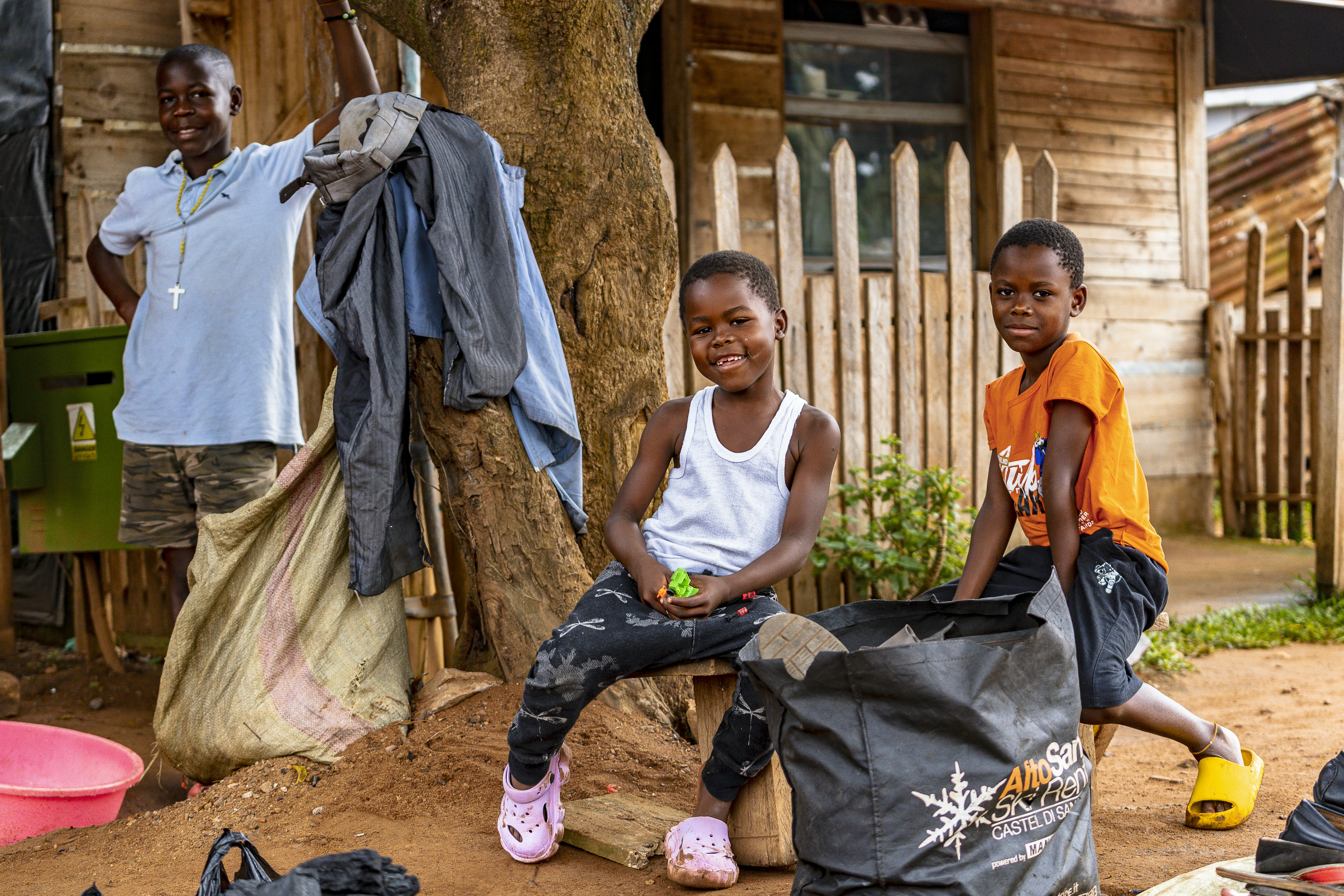 Two smiling children in front of a wooden house.