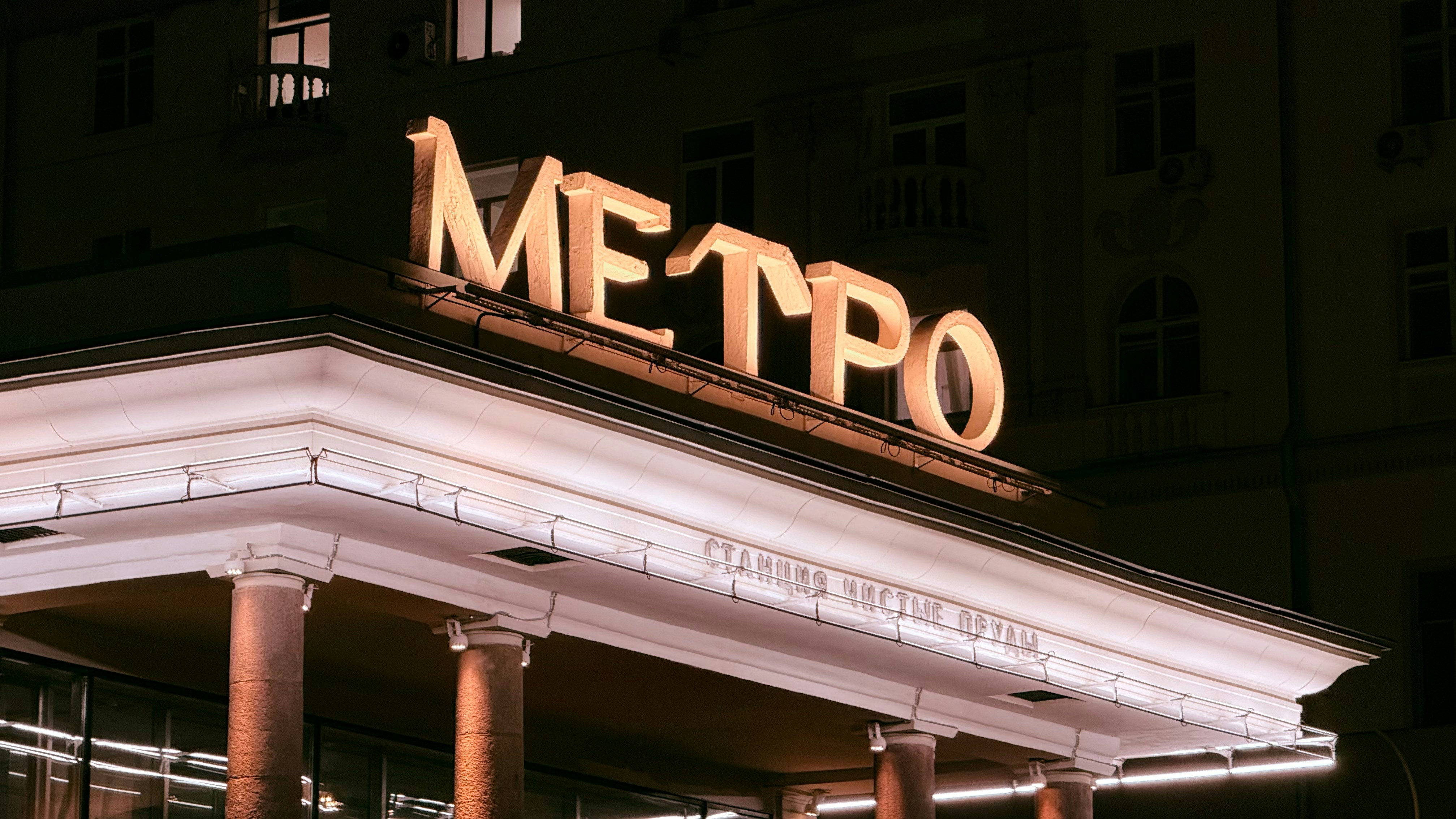 Lit metro sign above an entrance at night