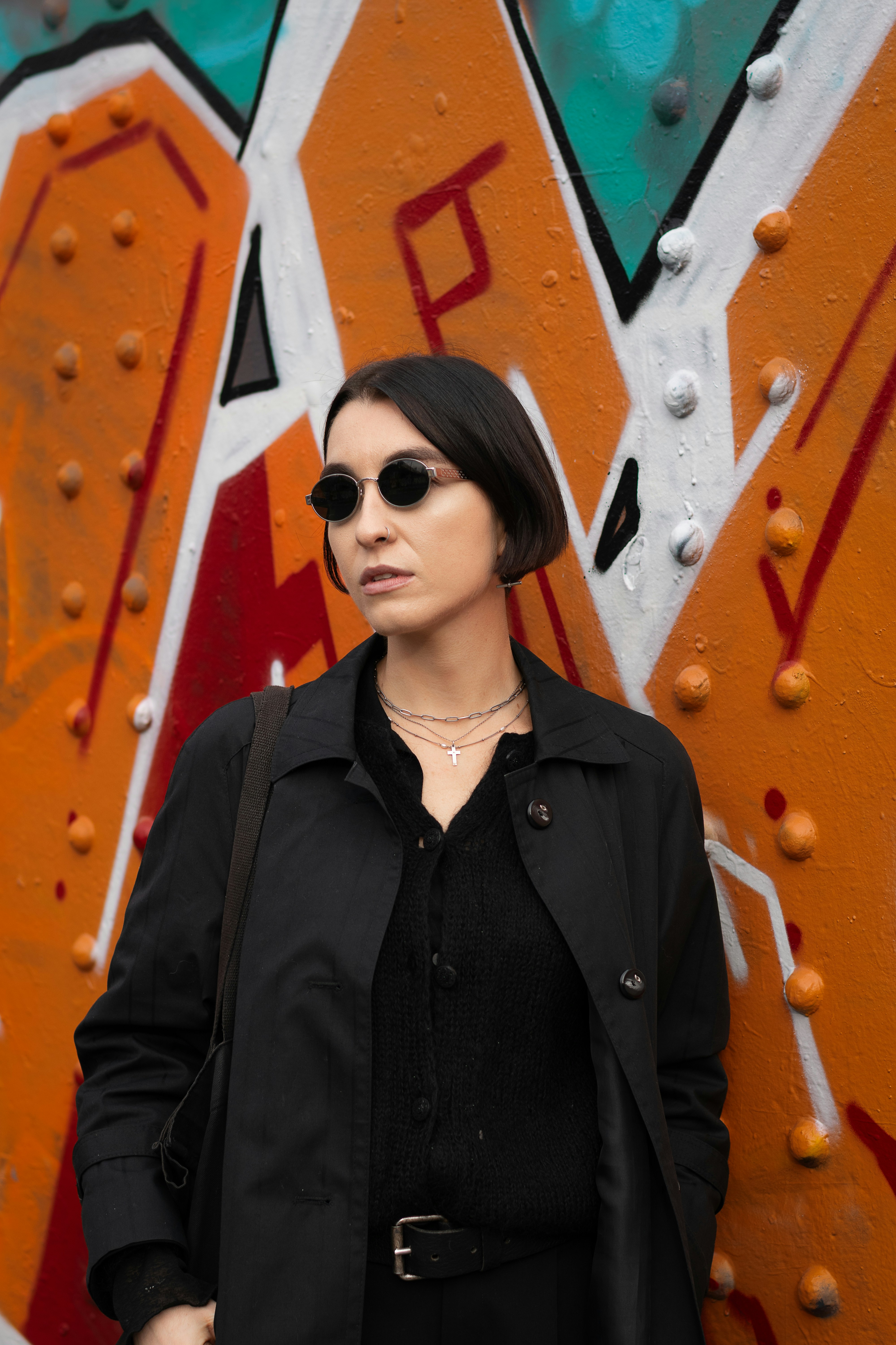 Woman in sunglasses stands against graffiti wall