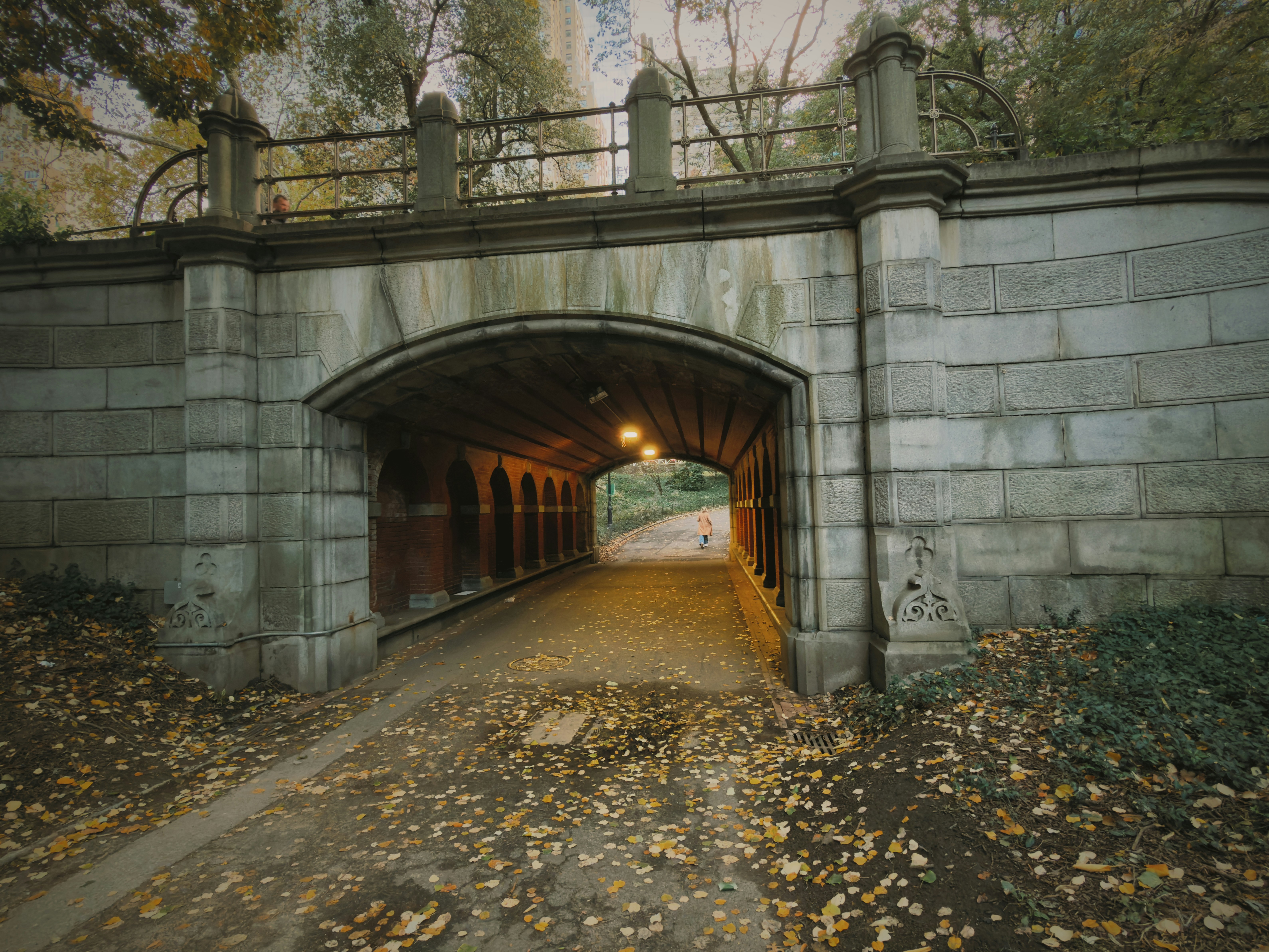 Stone bridge over a path covered in autumn leaves