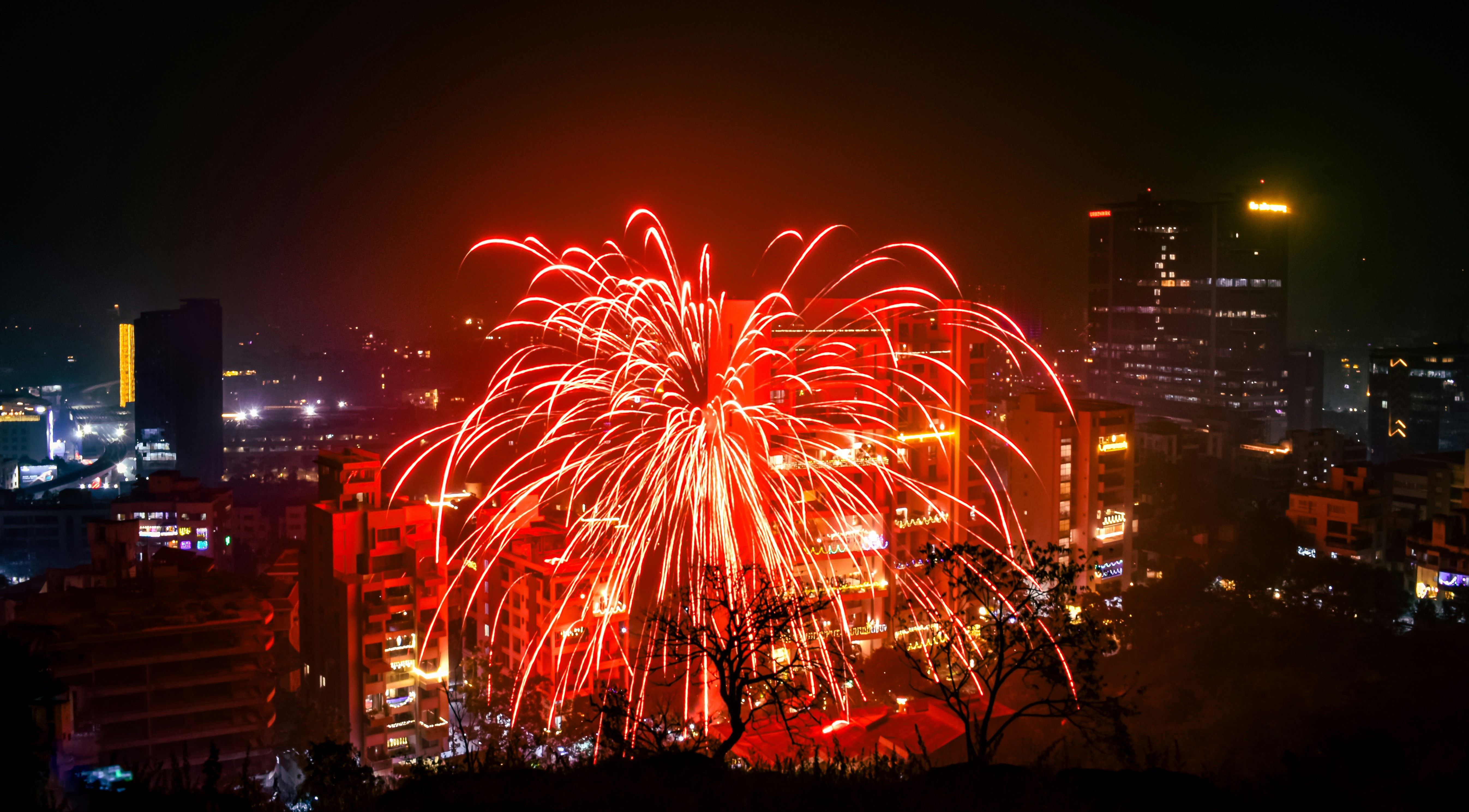 Bright red fireworks explode over a city skyline.