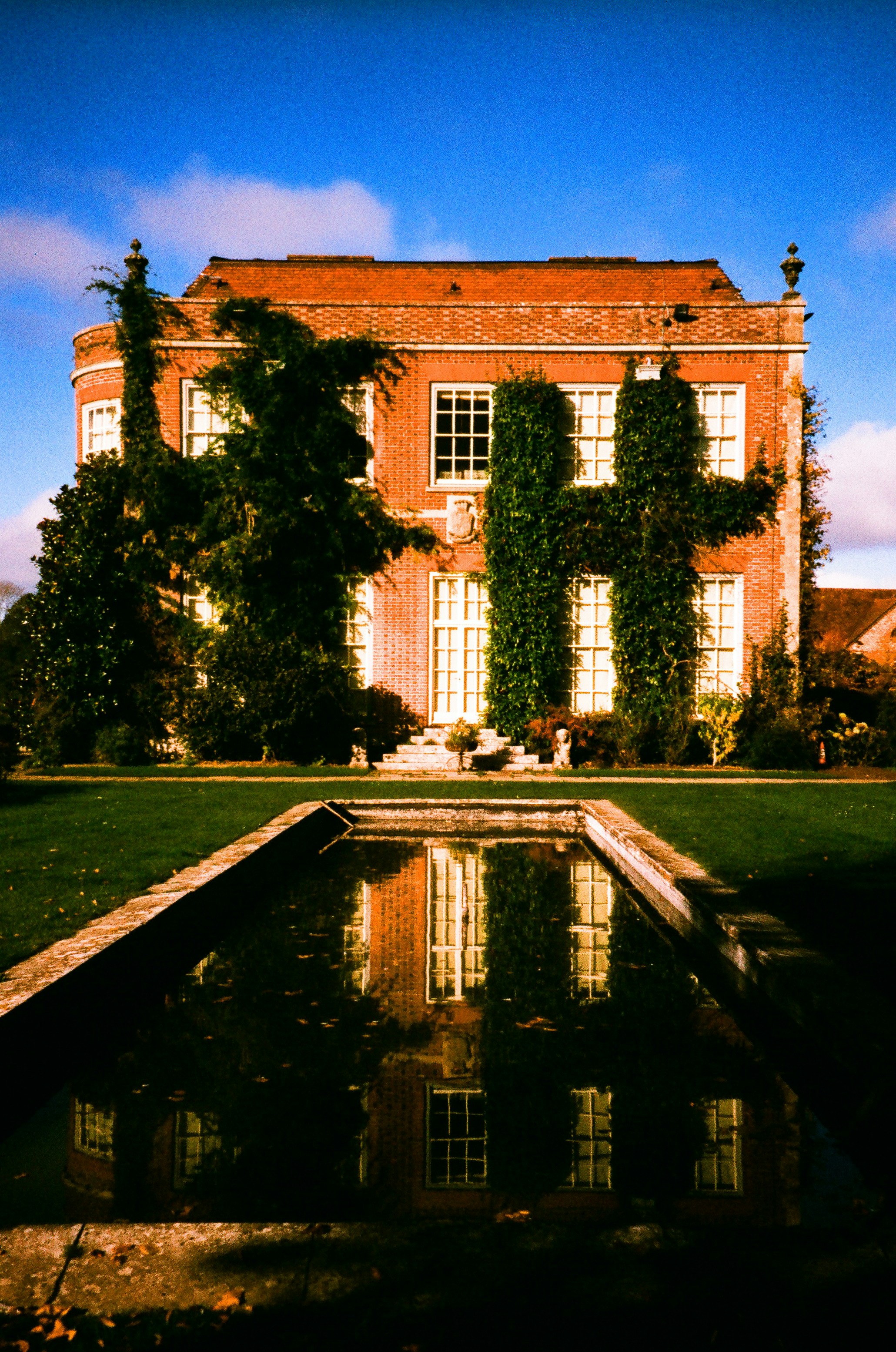 Casa señorial de ladrillo con hiedra reflejada en el agua