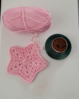 Pink yarn, star doily, and coffee cup on white surface