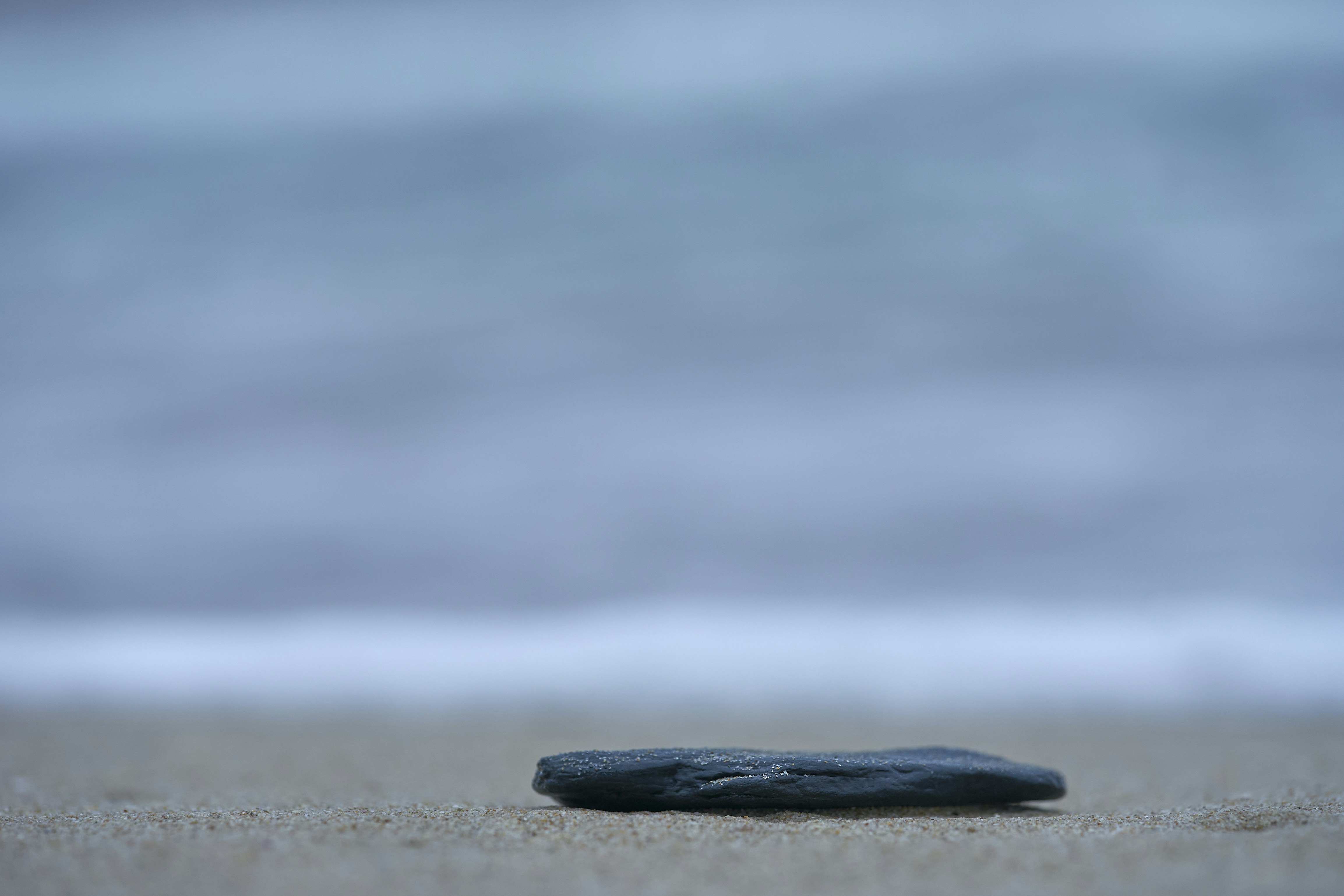 A single dark stone rests on a sandy beach.