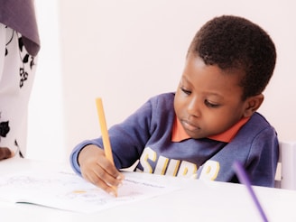 Young boy drawing with a yellow pencil at a table