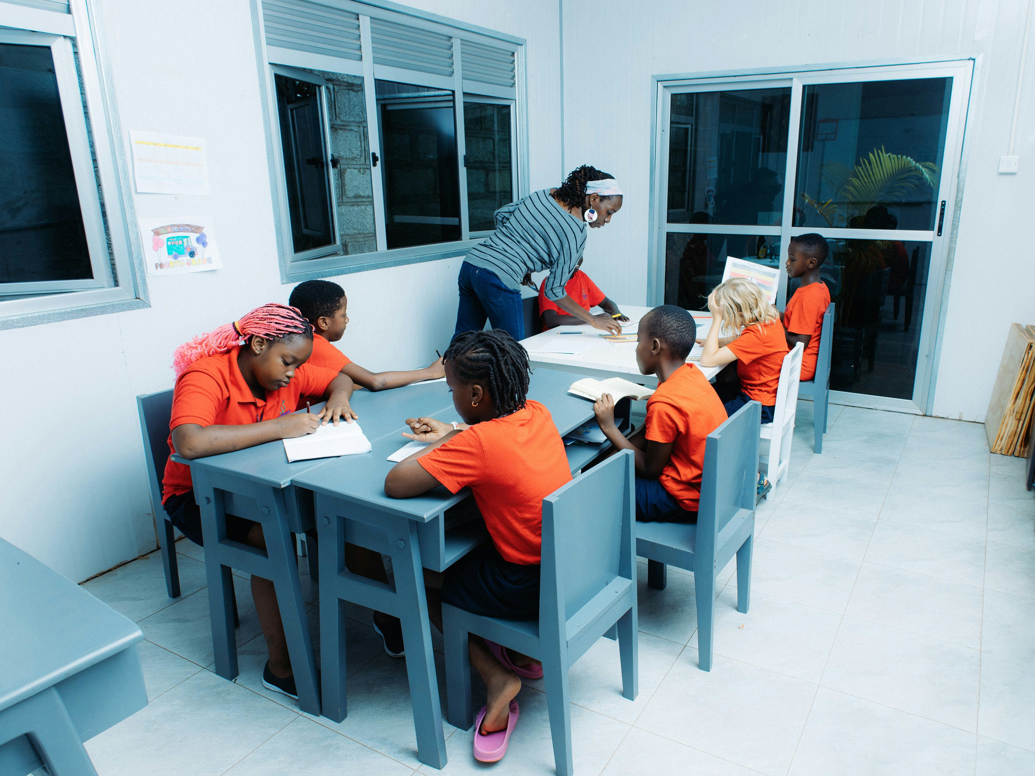 Teacher instructing children at tables in a classroom.
