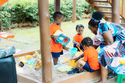 Children playing in a sandbox with an adult