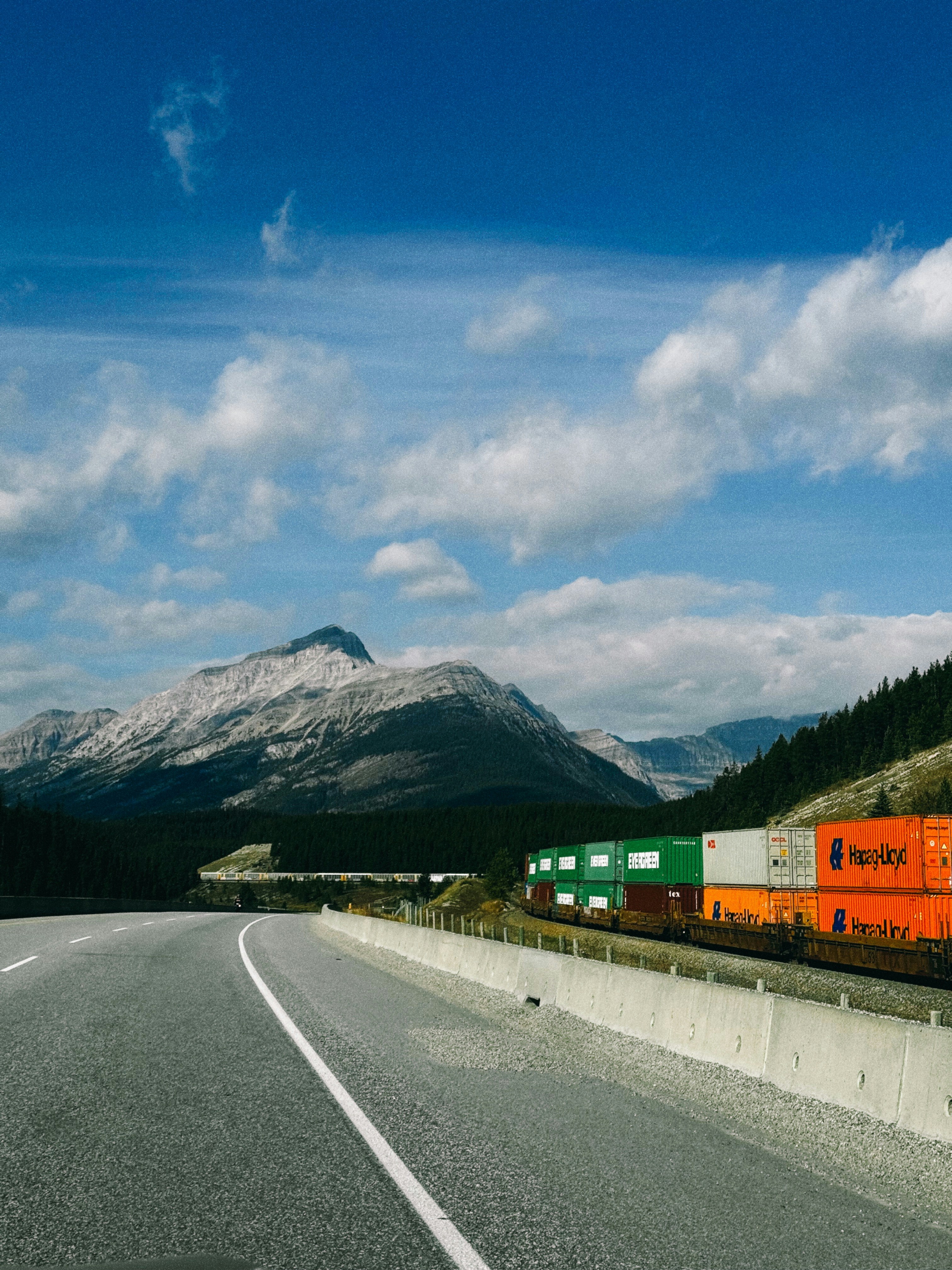 Freight train with colorful containers travels by mountains.