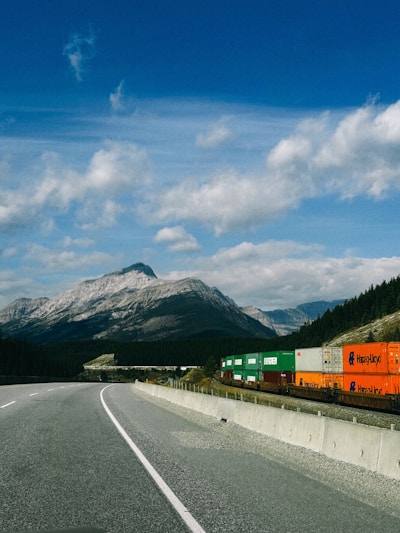 Freight train with colorful containers travels by mountains.