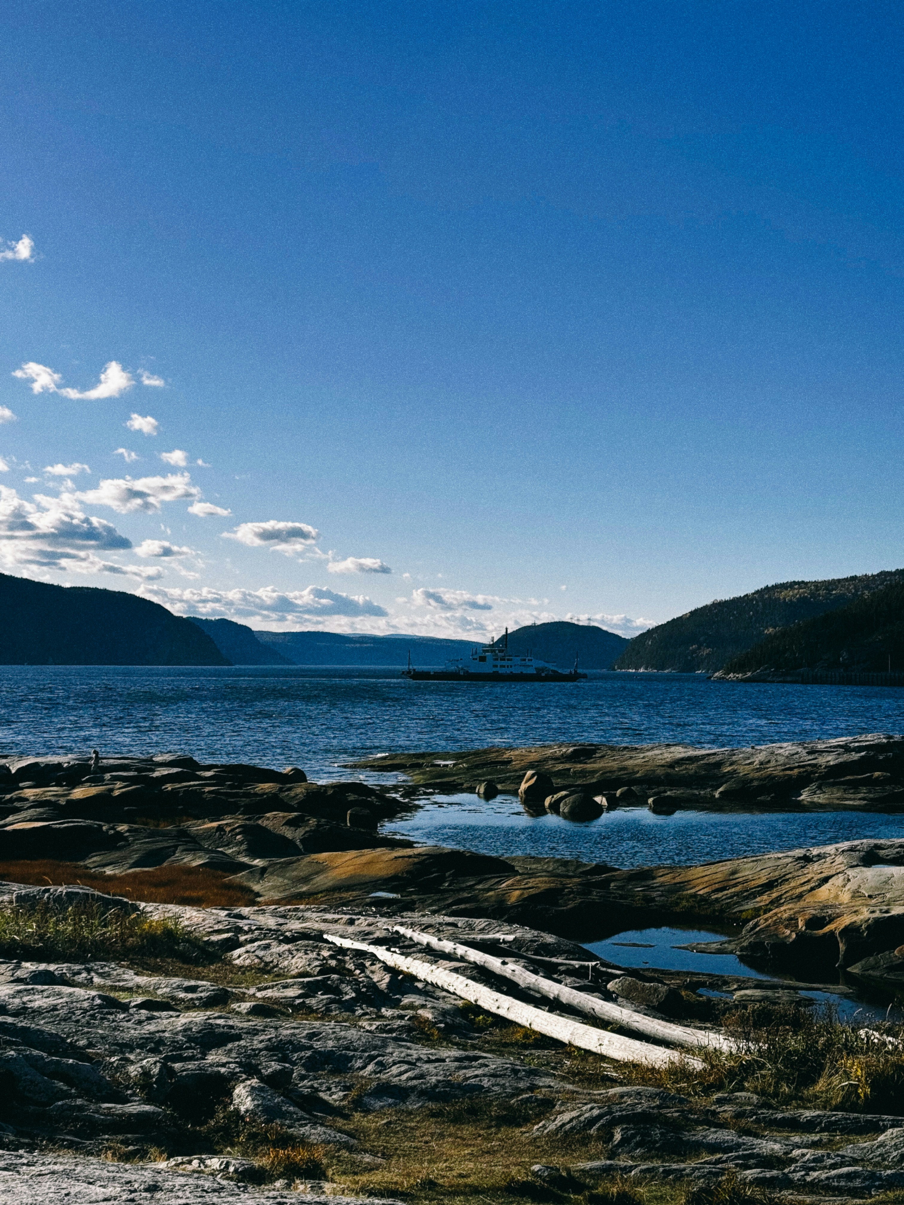 Rivage rocheux avec une eau bleue calme et des montagnes lointaines.