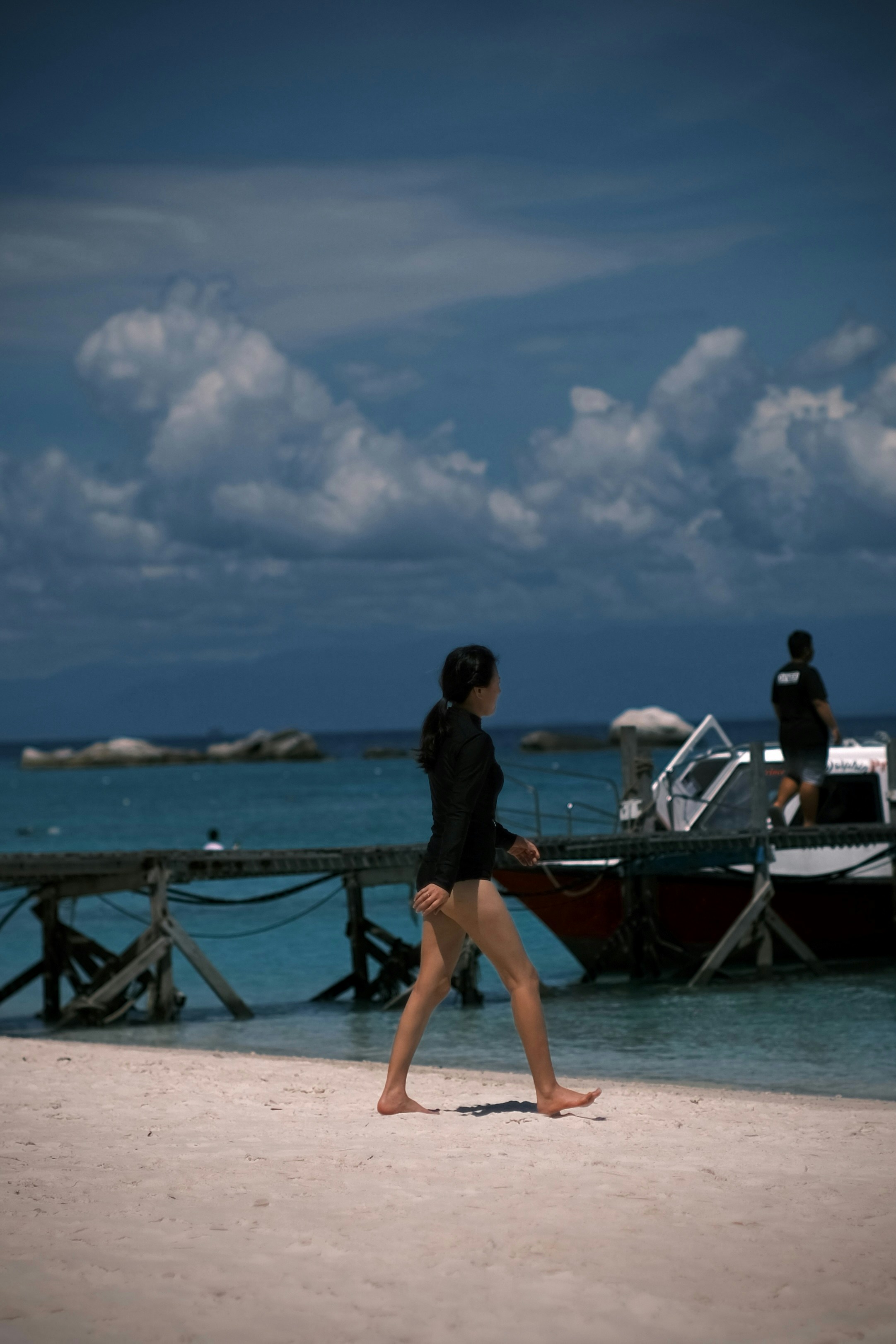 Woman walking on beach near wooden pier and boat