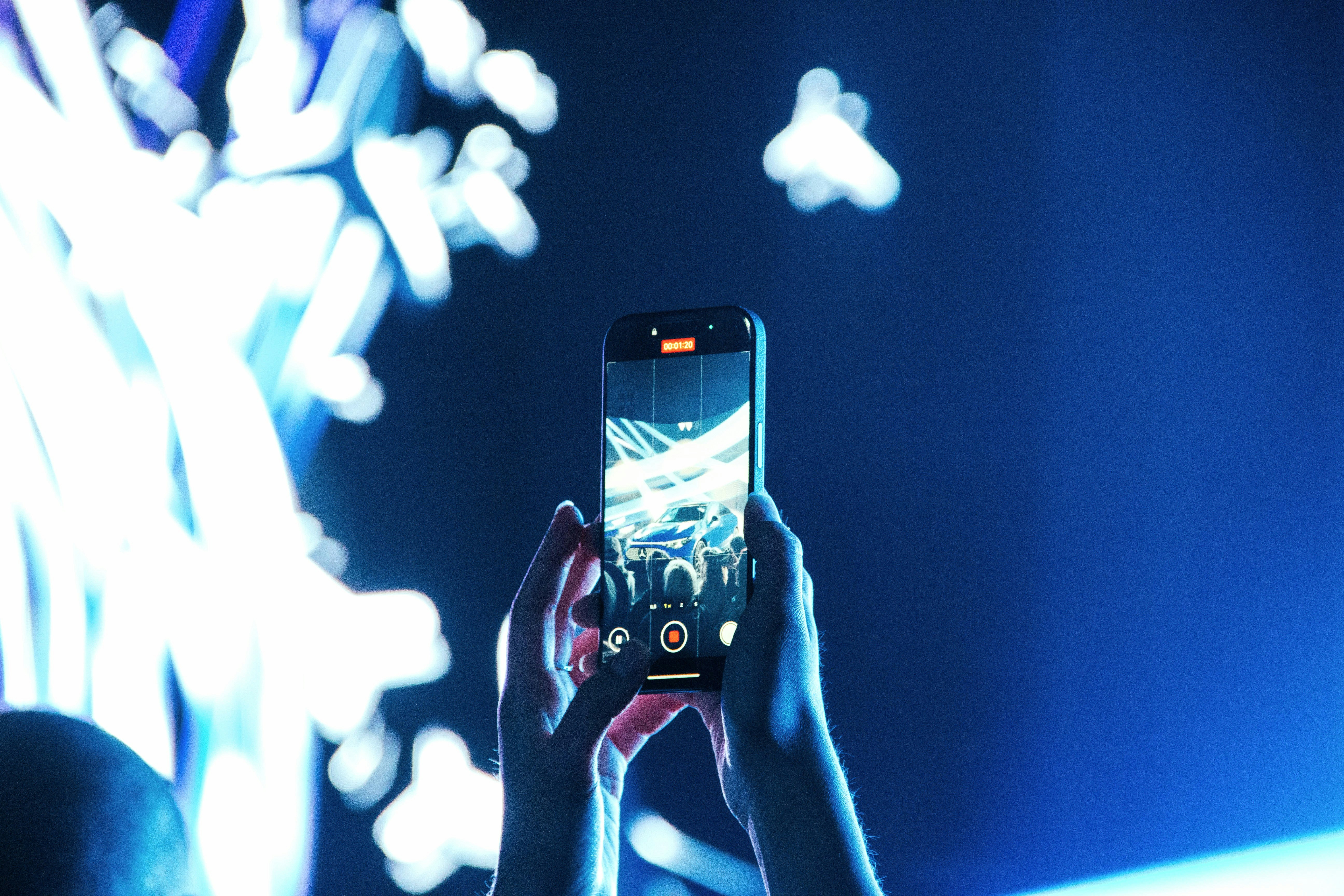 Person records concert with smartphone, blue lights