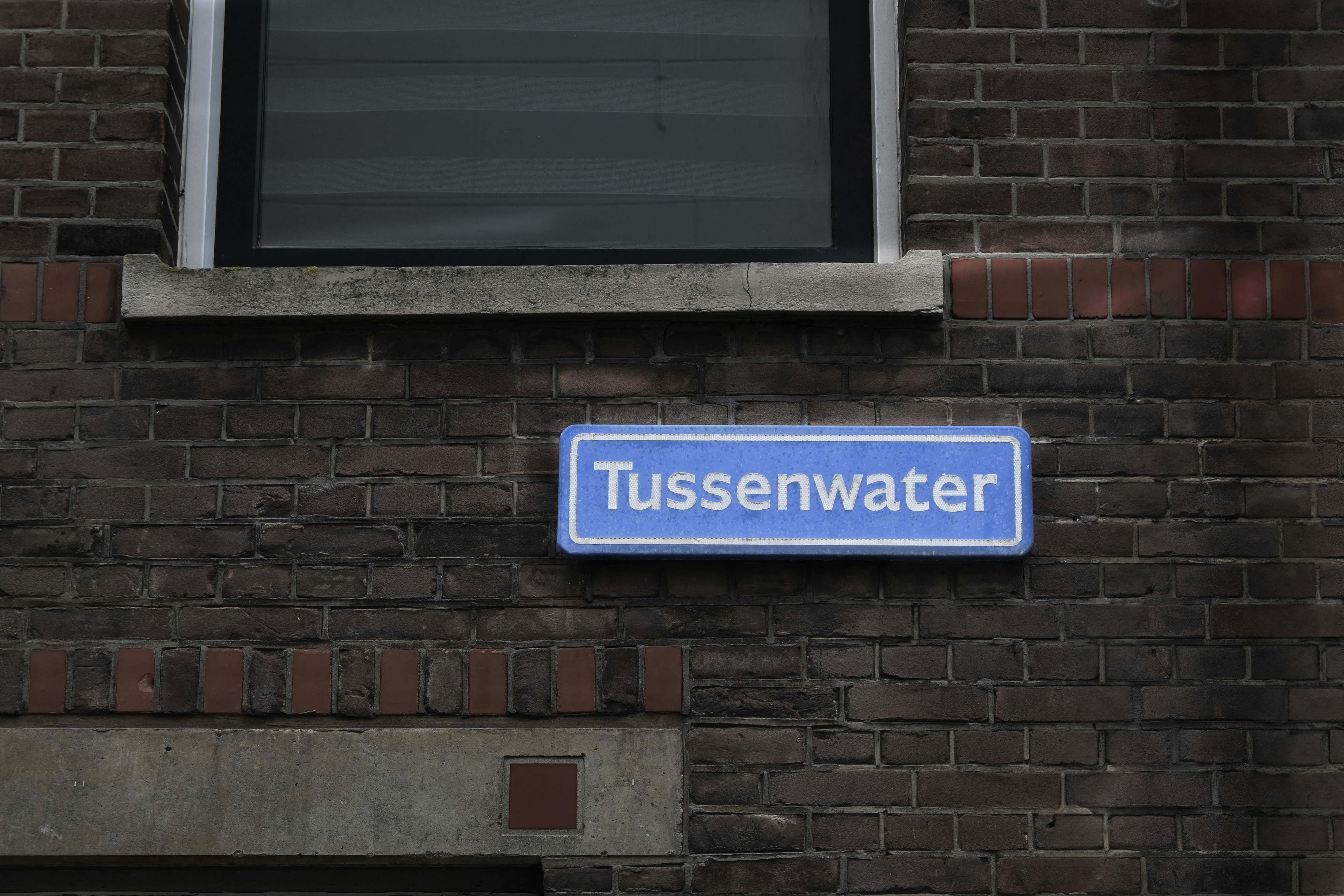 A blue street sign reads tussenwater on a brick wall.