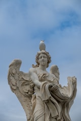 A seagull perched on an angel statue's head.