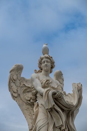 A seagull perched on an angel statue's head.