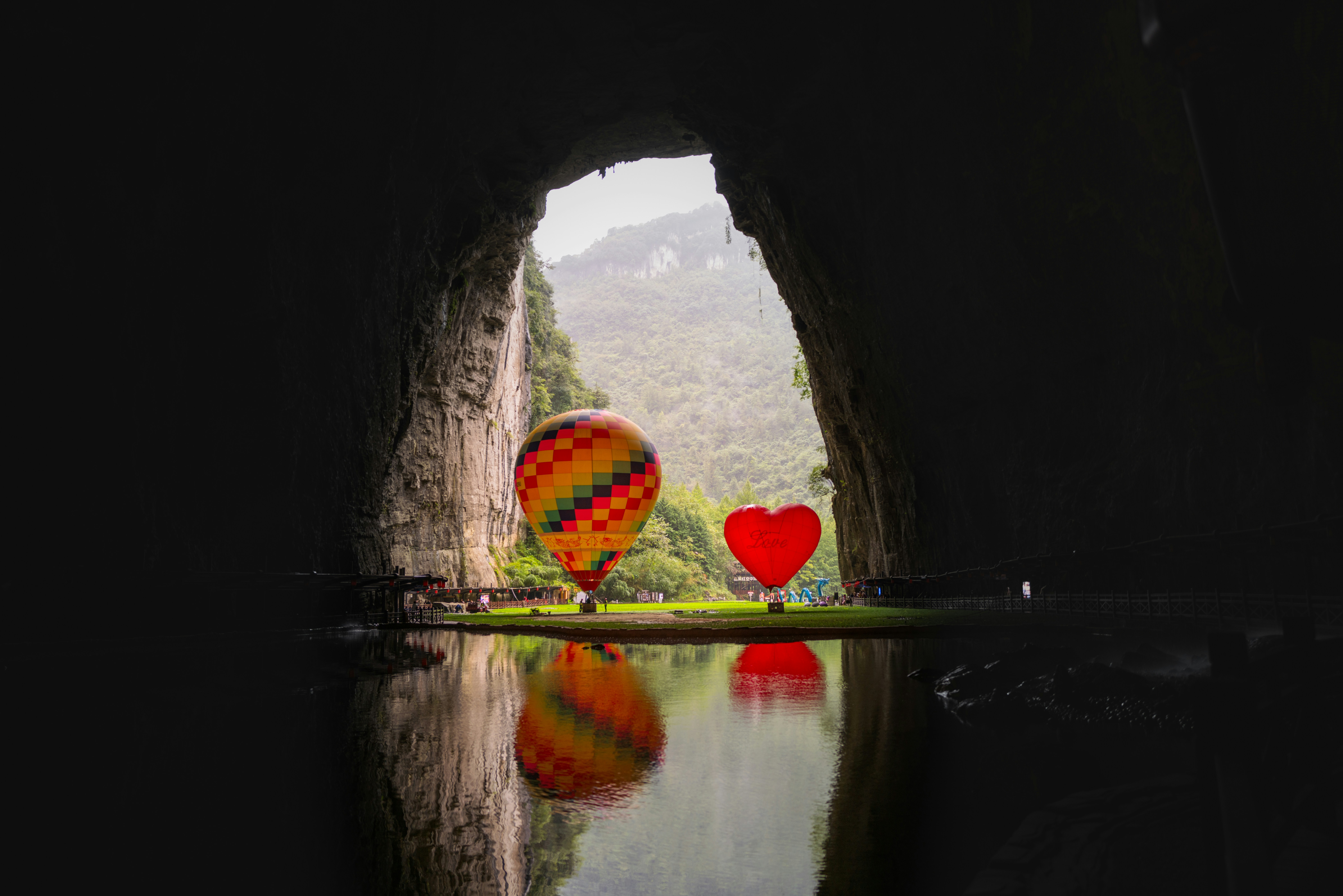 Two hot air balloons reflected in water inside cave