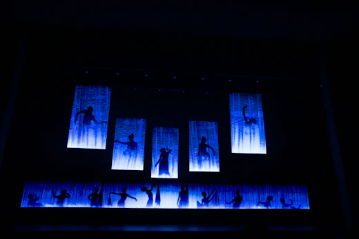 Silhouettes of dancers on a blue illuminated stage.