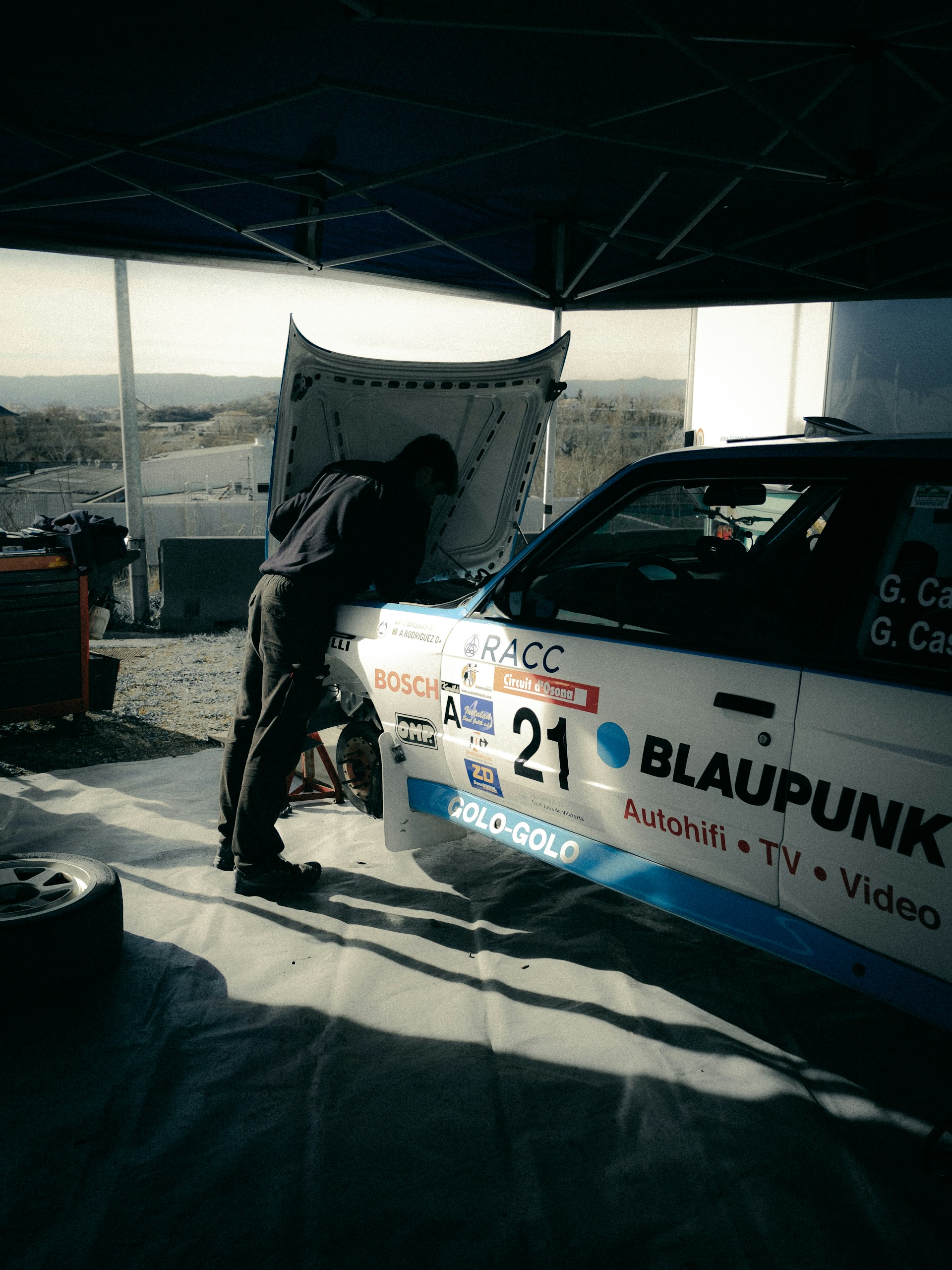 Mechanic working on race car engine under canopy