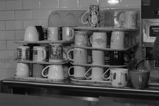 Various mugs stacked on shelves behind counter.