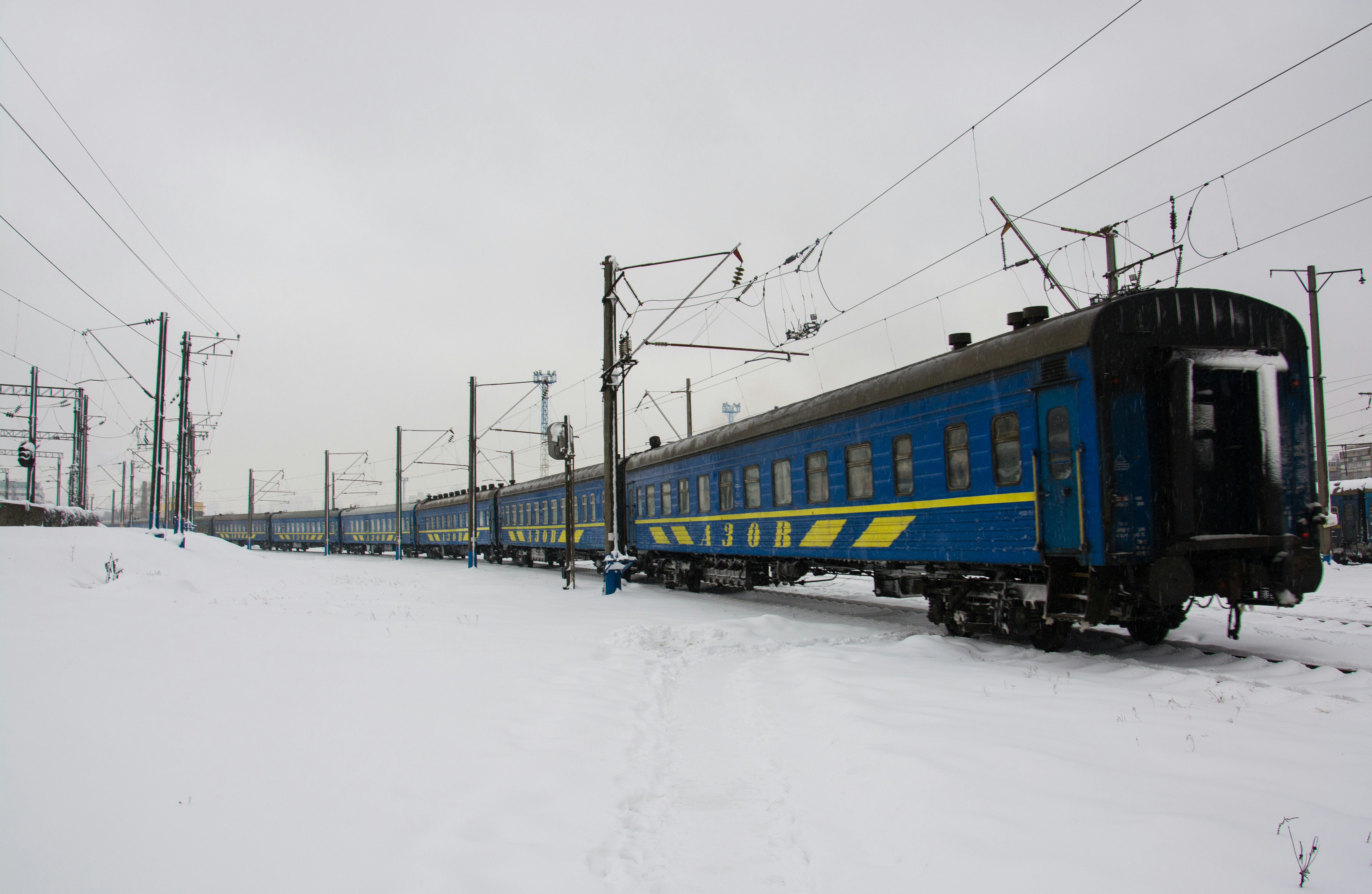Blue train cars on snowy tracks under cloudy sky