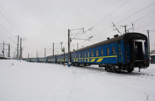 Blue train cars on snowy tracks under cloudy sky