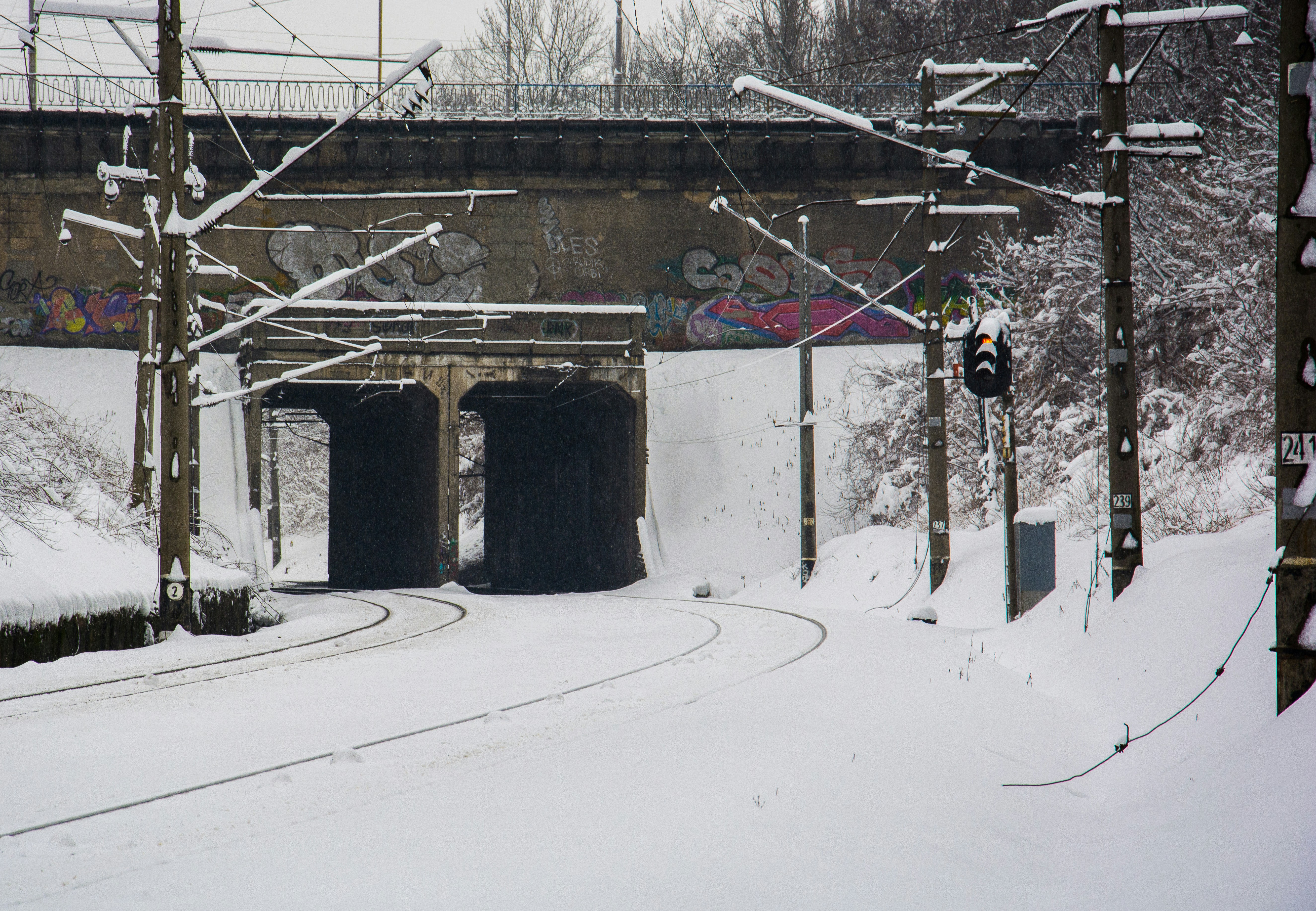 Snow covered train tracks under a bridge